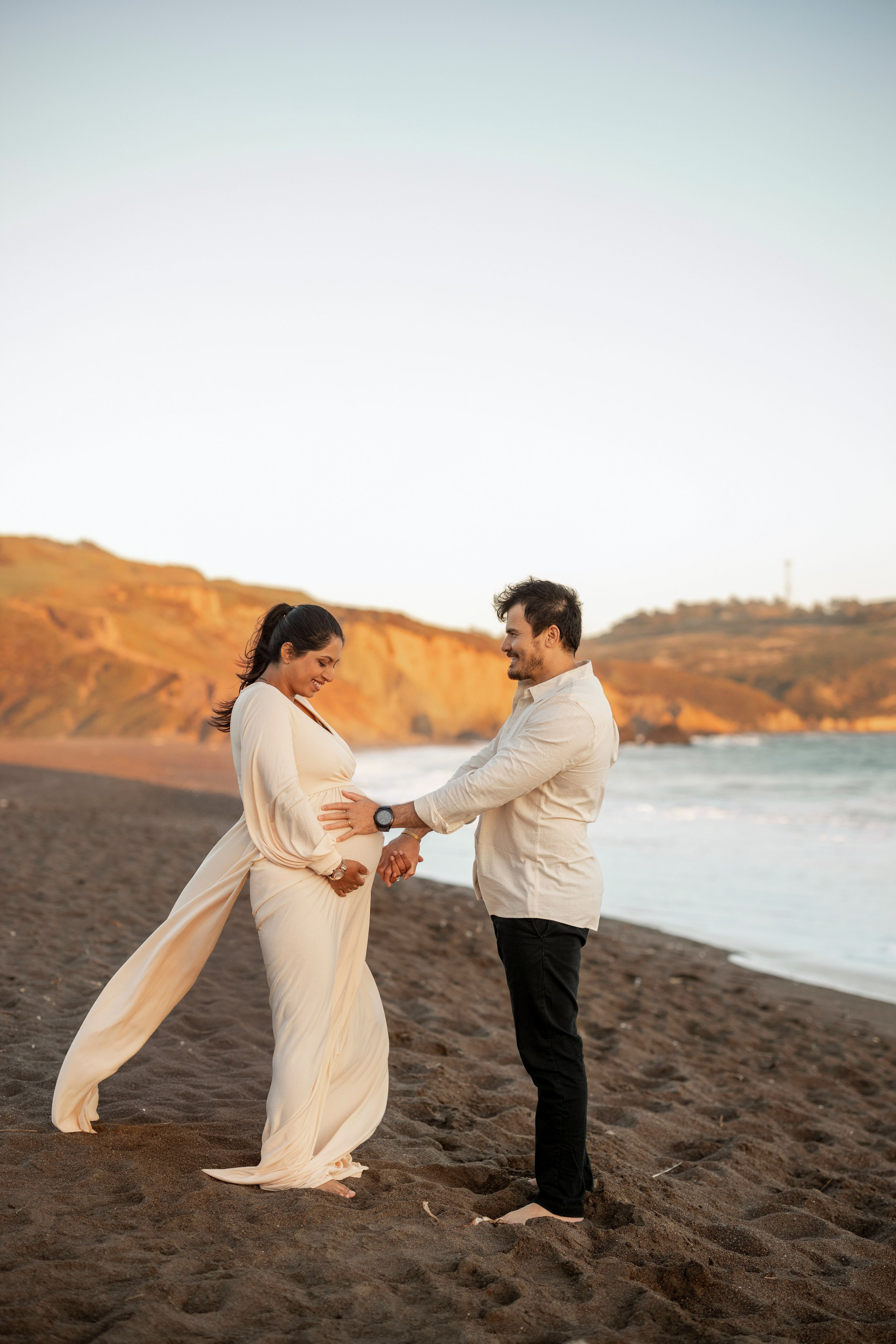 Pregnant woman in flowing dress with husband on sandy beach