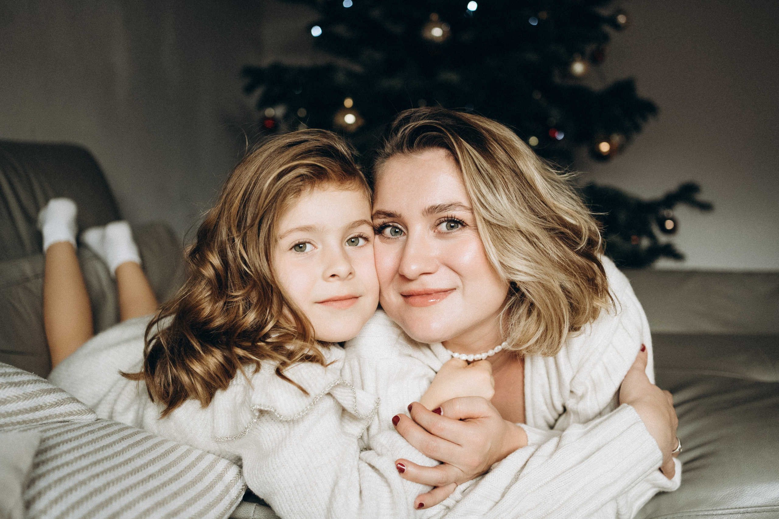Mutter und Tochter kuscheln sich auf der Sofa und schauen liebevoll in die Kamera.