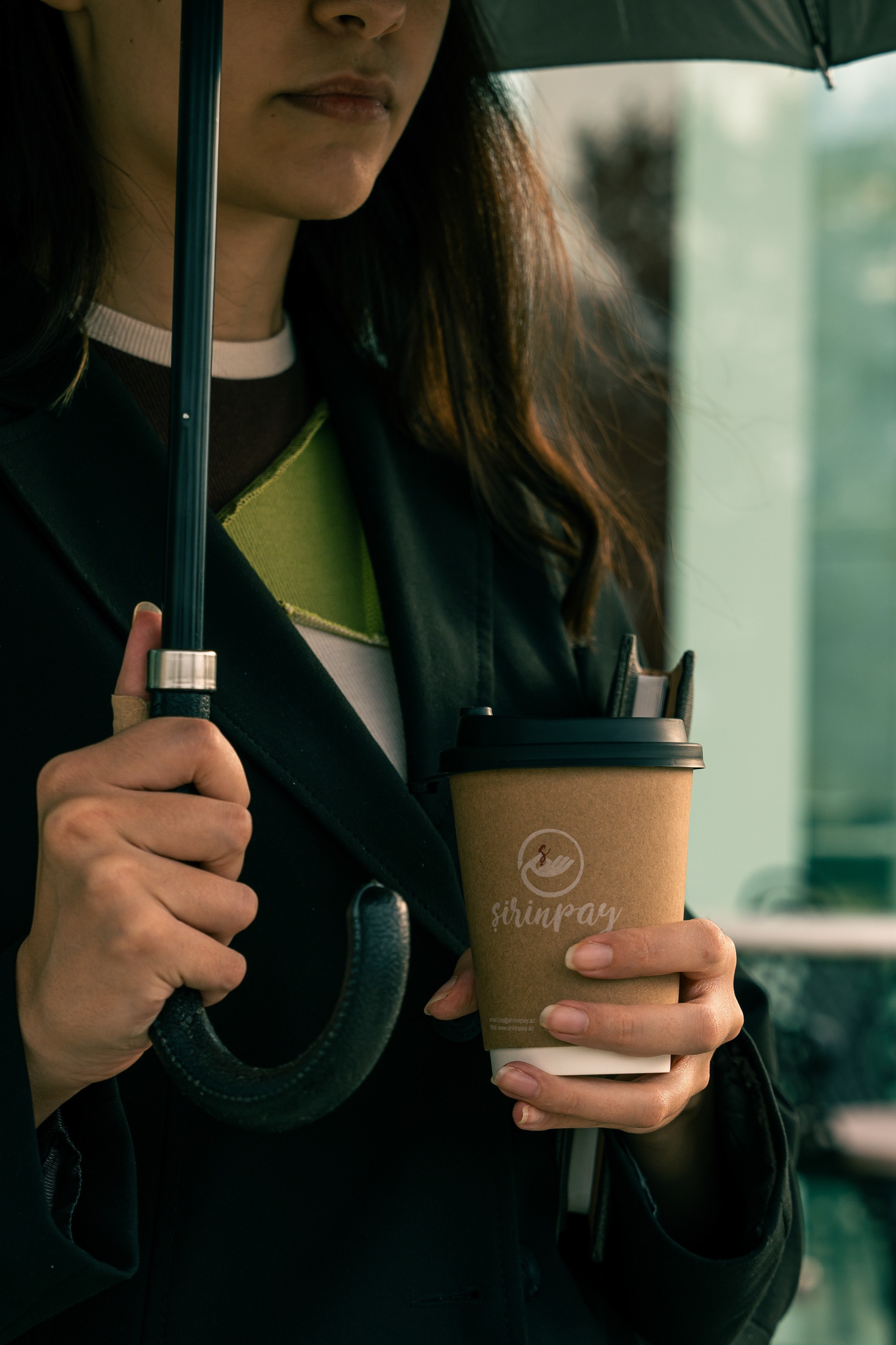 Rahat və yağışlı bir günü təmsil edən "Şirinpay"dan qəhvə fincanı və qara çətir tutan şəxs.