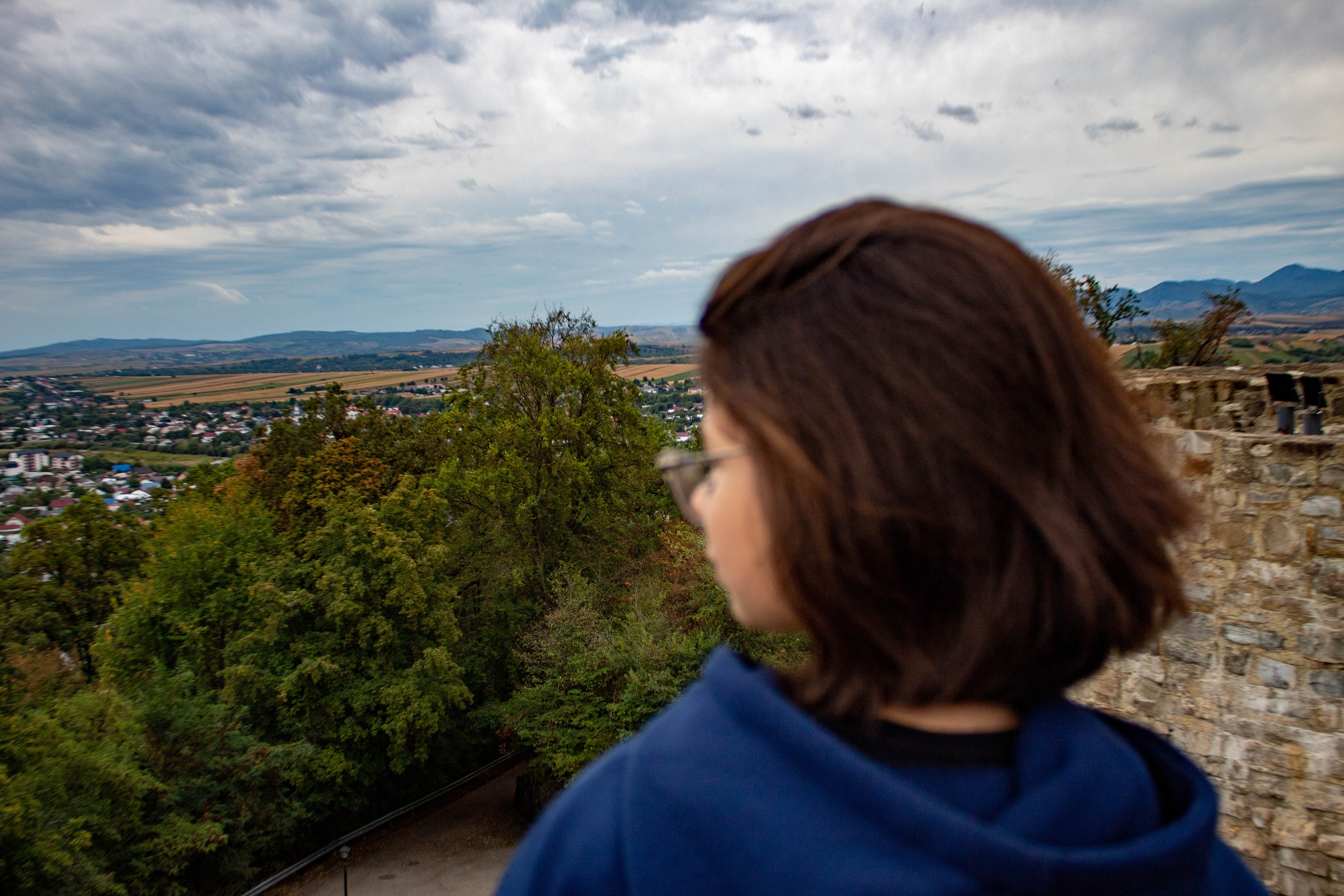 Woman standing at a mountain viewpoint overlooking foggy peaks at sunset.