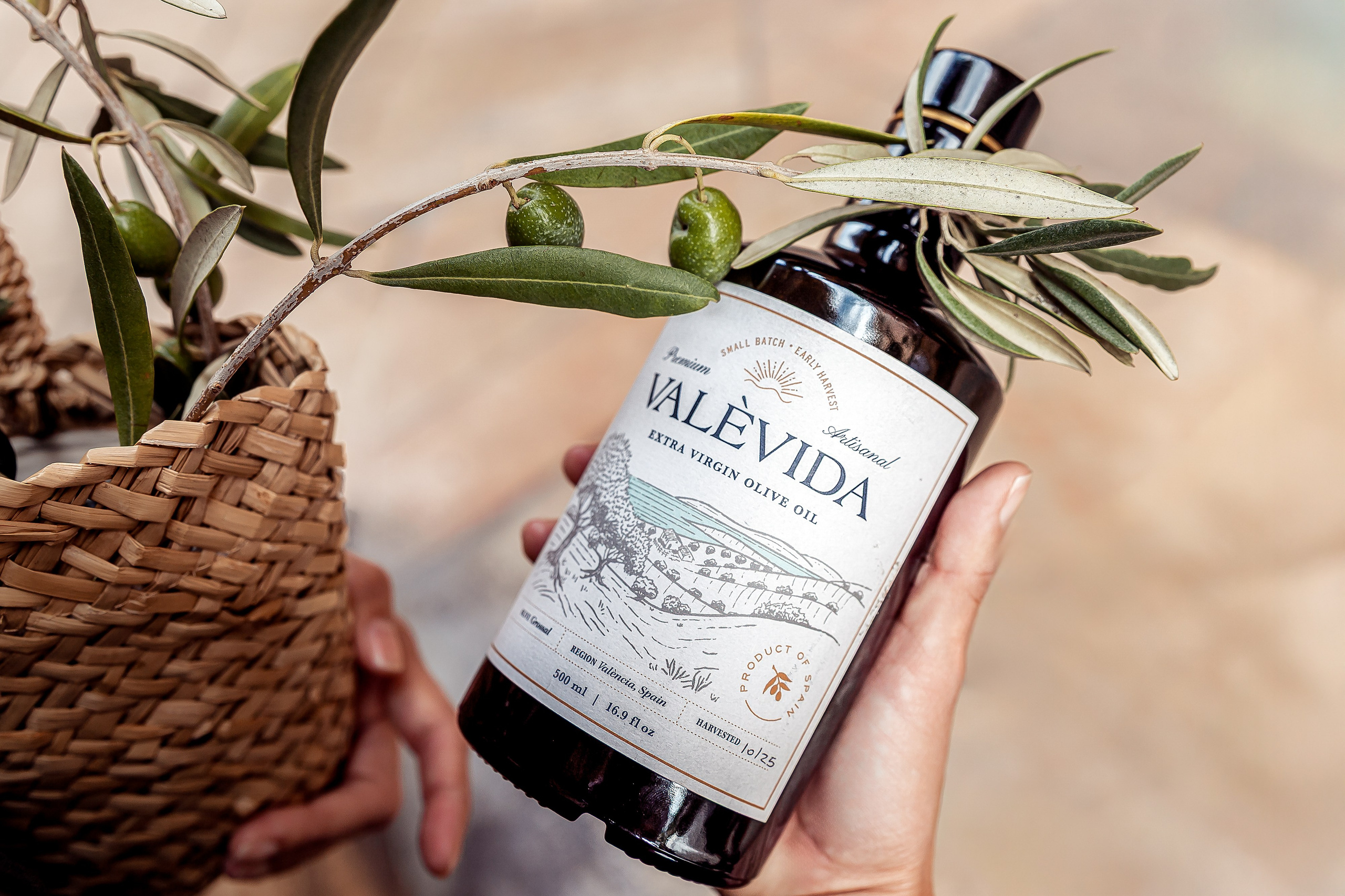 Product branding photo taken in Valencia, Spain, showcasing a bottle of premium olive oil held beside fresh olive branches and a rustic woven basket — ideal for businesses seeking natural, artisanal product photography and brand content in Valencia or across Spain.