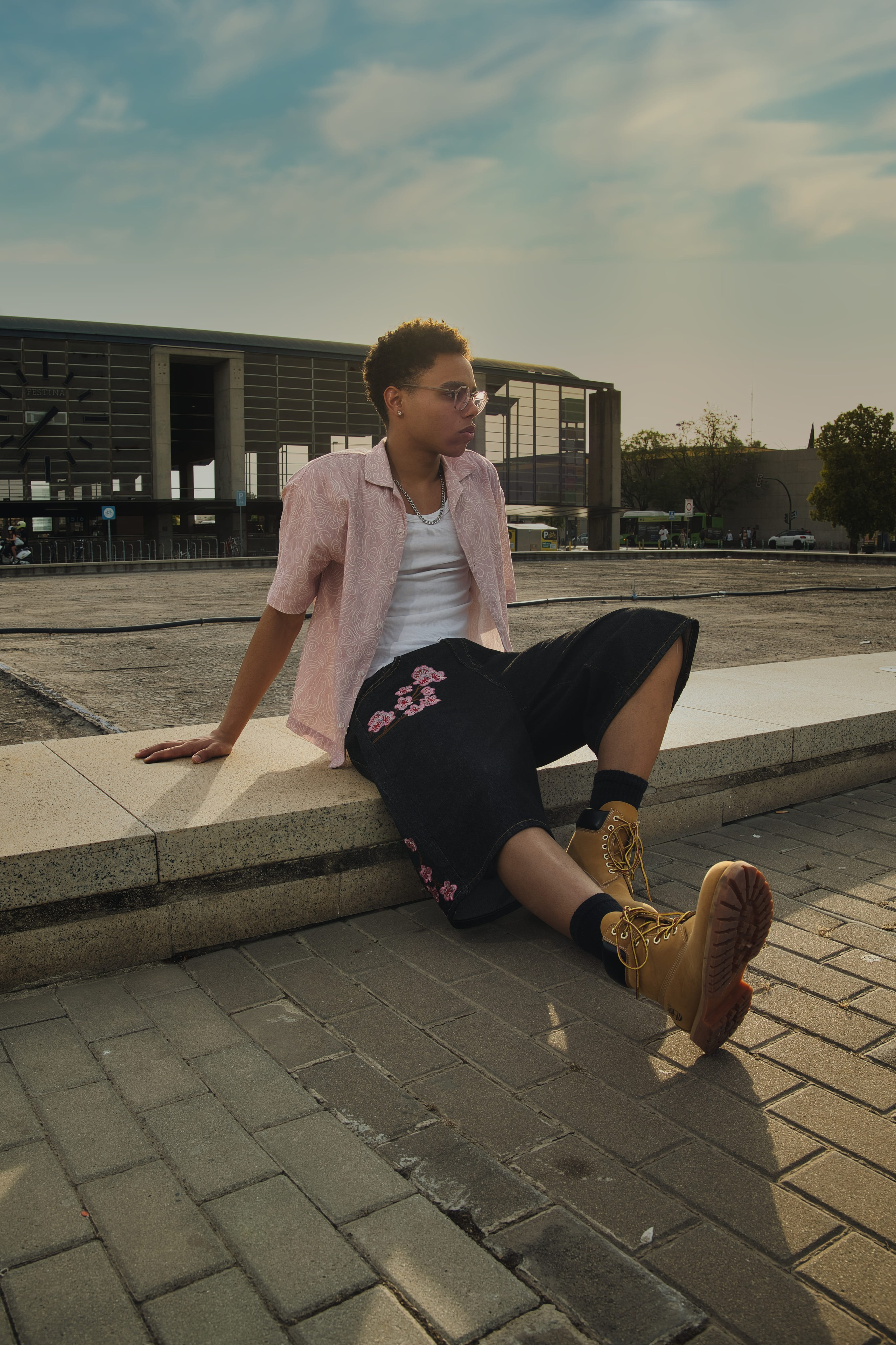 Primer plano de un joven con gafas luciendo un outfit casual de streetwear con accesorios.