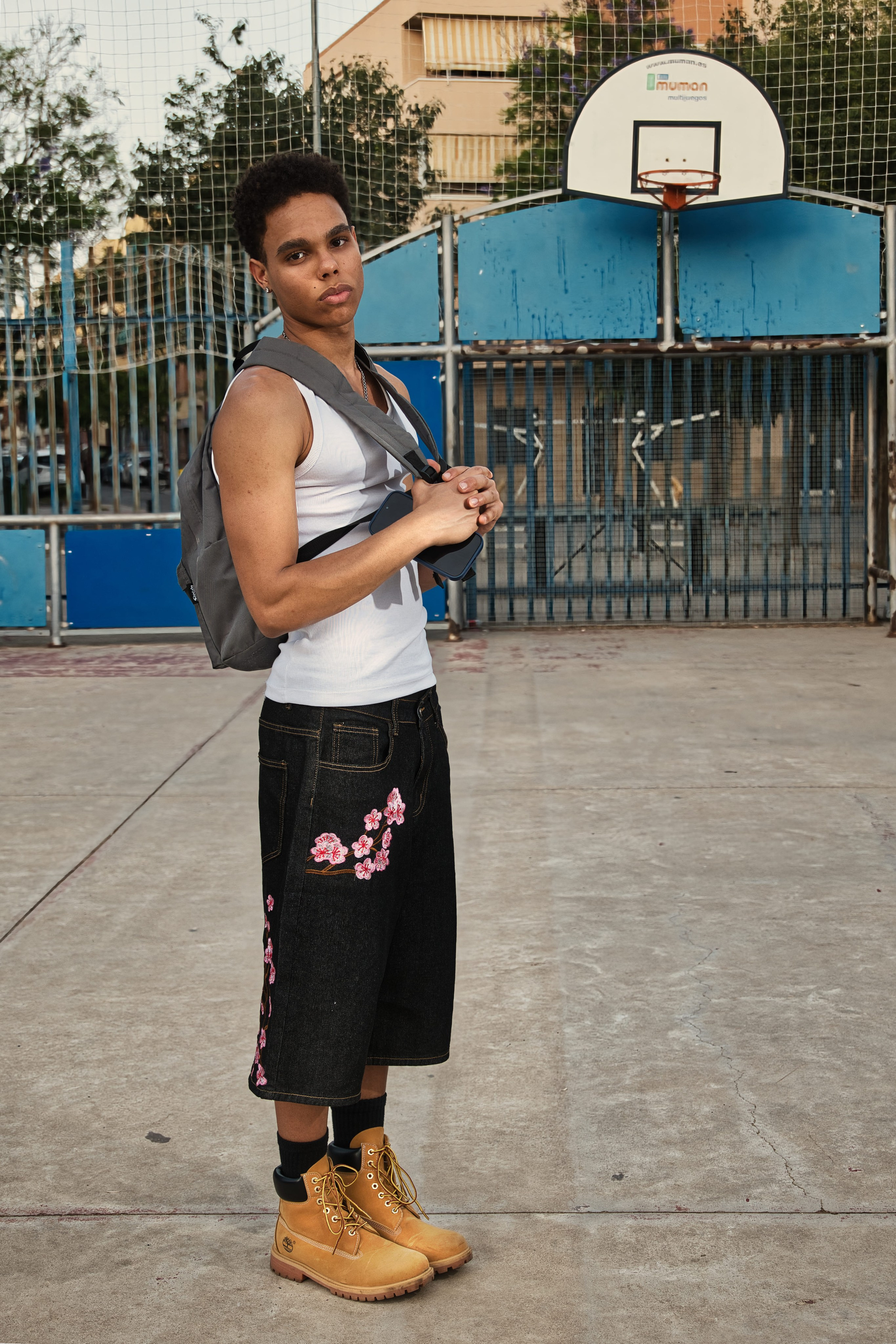 Look deportivo urbano con bermudas denim oscuras con bordados florales, botas y mochila gris.