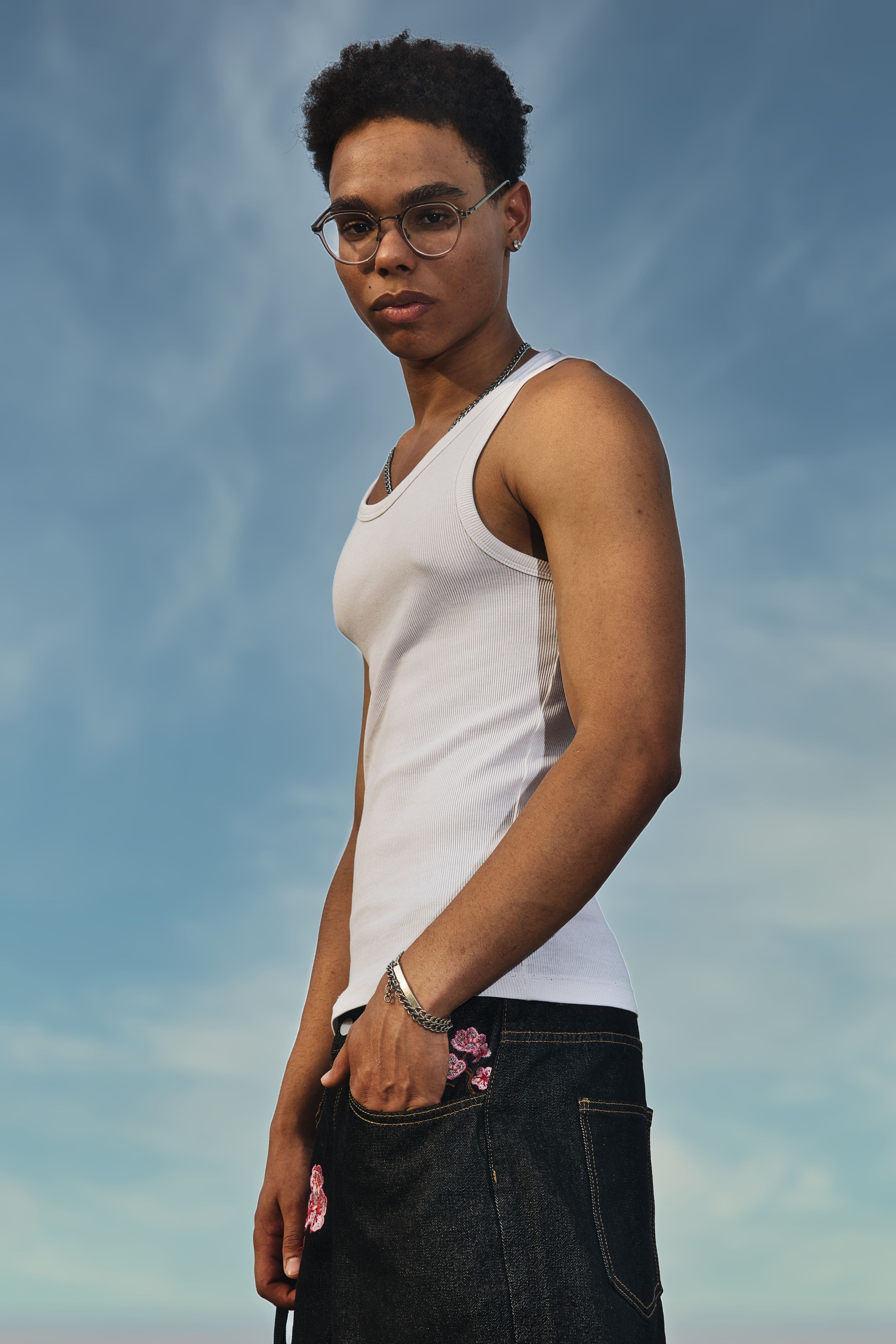 Posa con gafas luciendo un look de streetwear casual con camiseta de tirantes y collar.