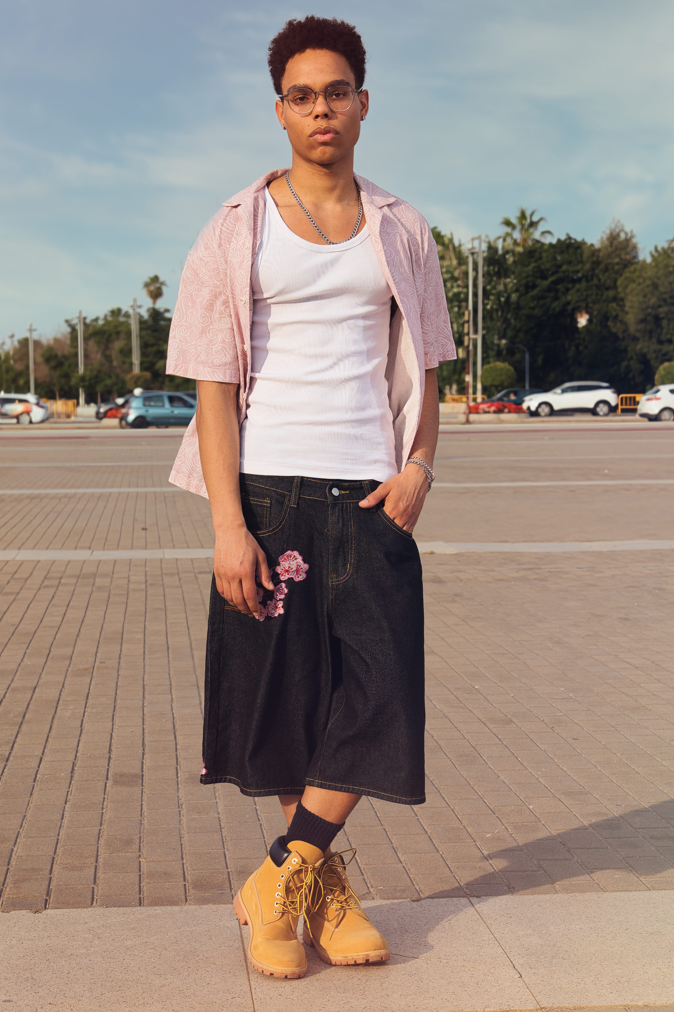Joven con gafas posa con una expresión seria luciendo un outfit urbano con accesorios.