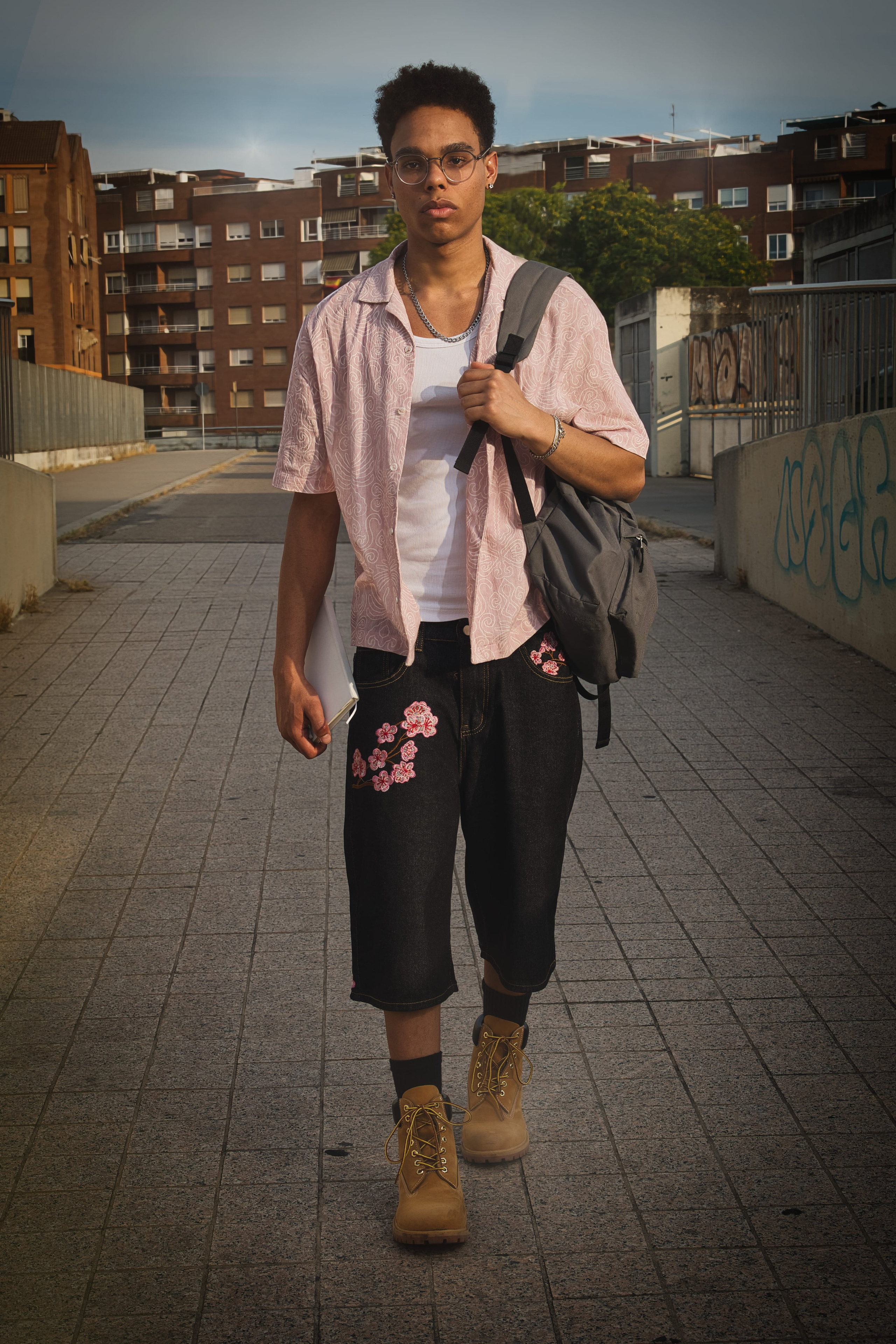 Joven camina con confianza por la ciudad luciendo un look de streetwear con mochila y portátil.
