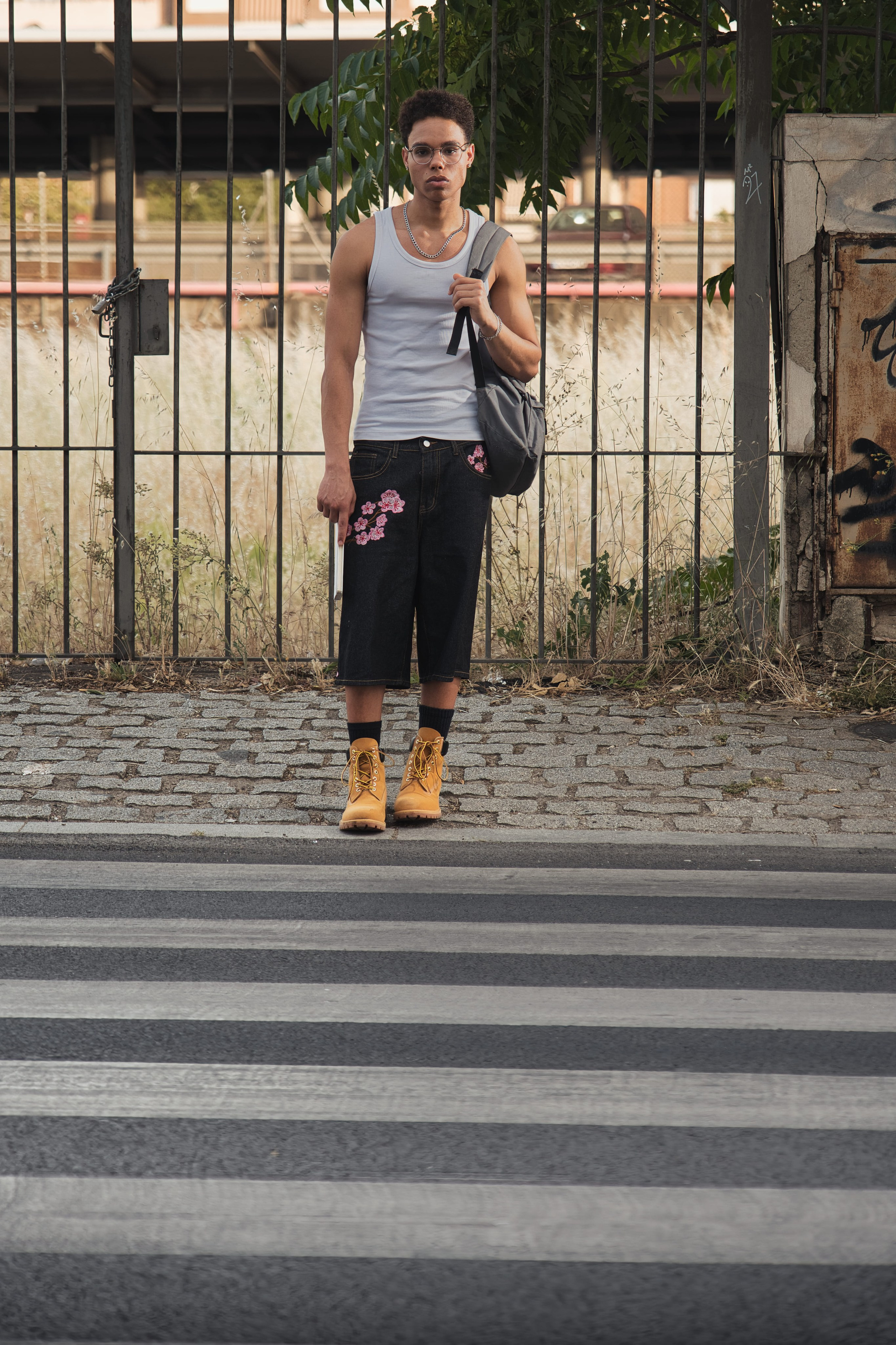 Look completo de moda masculina con bermudas vaqueras bordadas, botas amarillas y mochila al hombro.