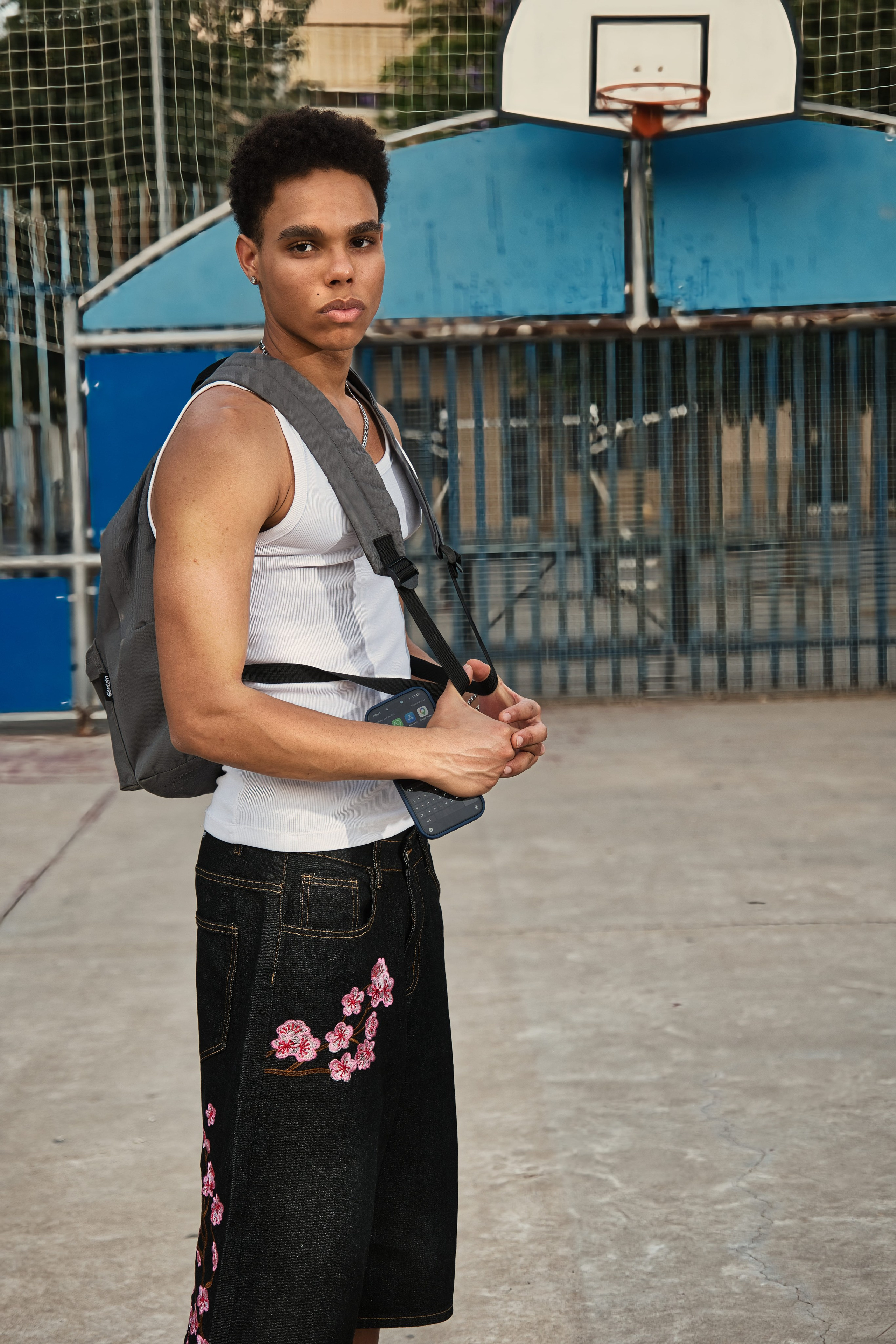Fotografía de modelo masculino luciendo camiseta de tirantes blanca y cadena de plata en una cancha exterior.