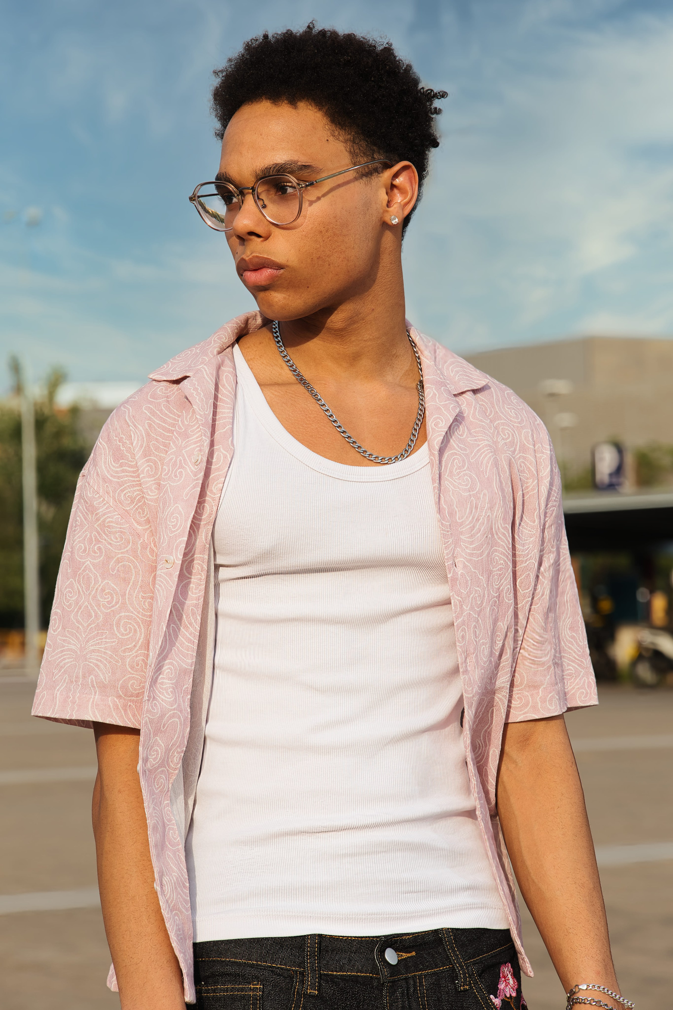Joven con gafas posa con una expresión seria luciendo un outfit urbano con accesorios.