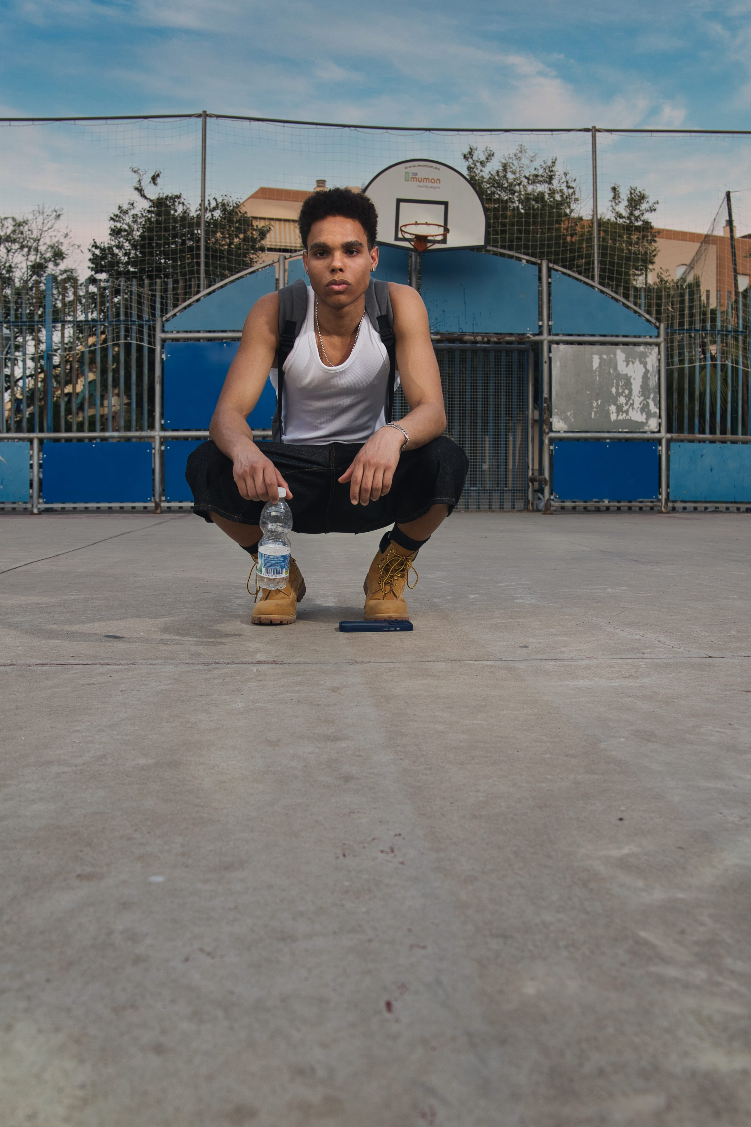 Fotografía de moda masculina en cancha de baloncesto con botella de agua, botas de montaña y bermudas denim.