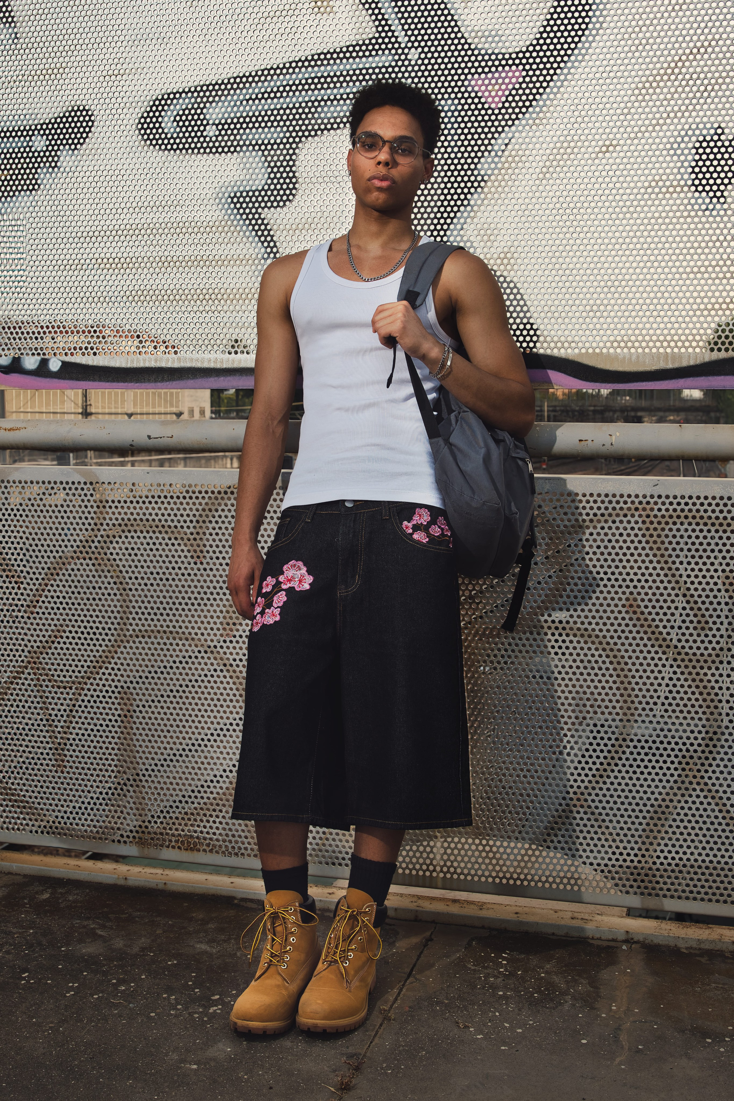 Look completo de streetwear para hombre con camiseta de tirantes, shorts vaqueros bordados y botas.