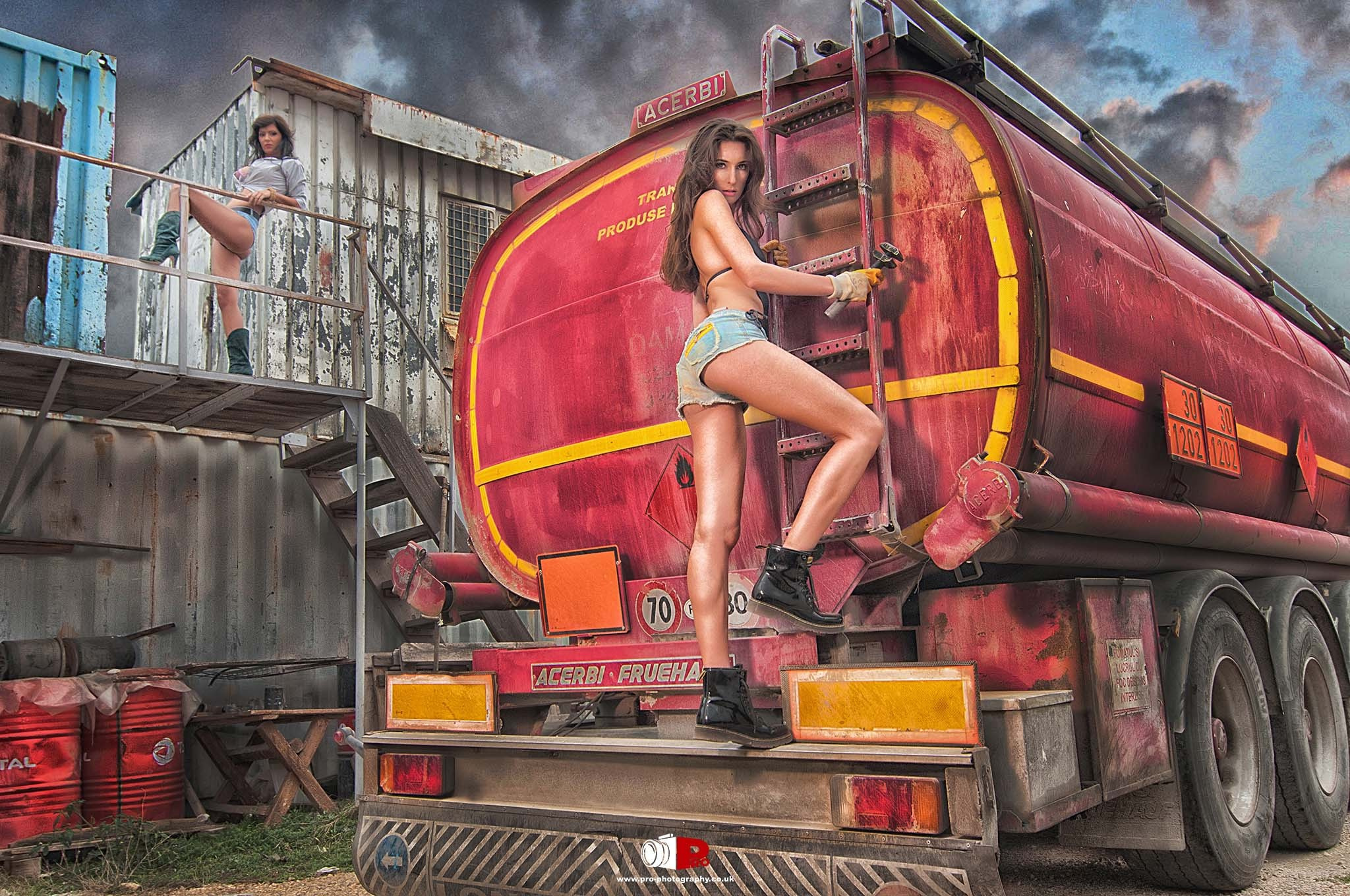 Model posing confidently in front of a red fuel tanker in an industrial setting.
