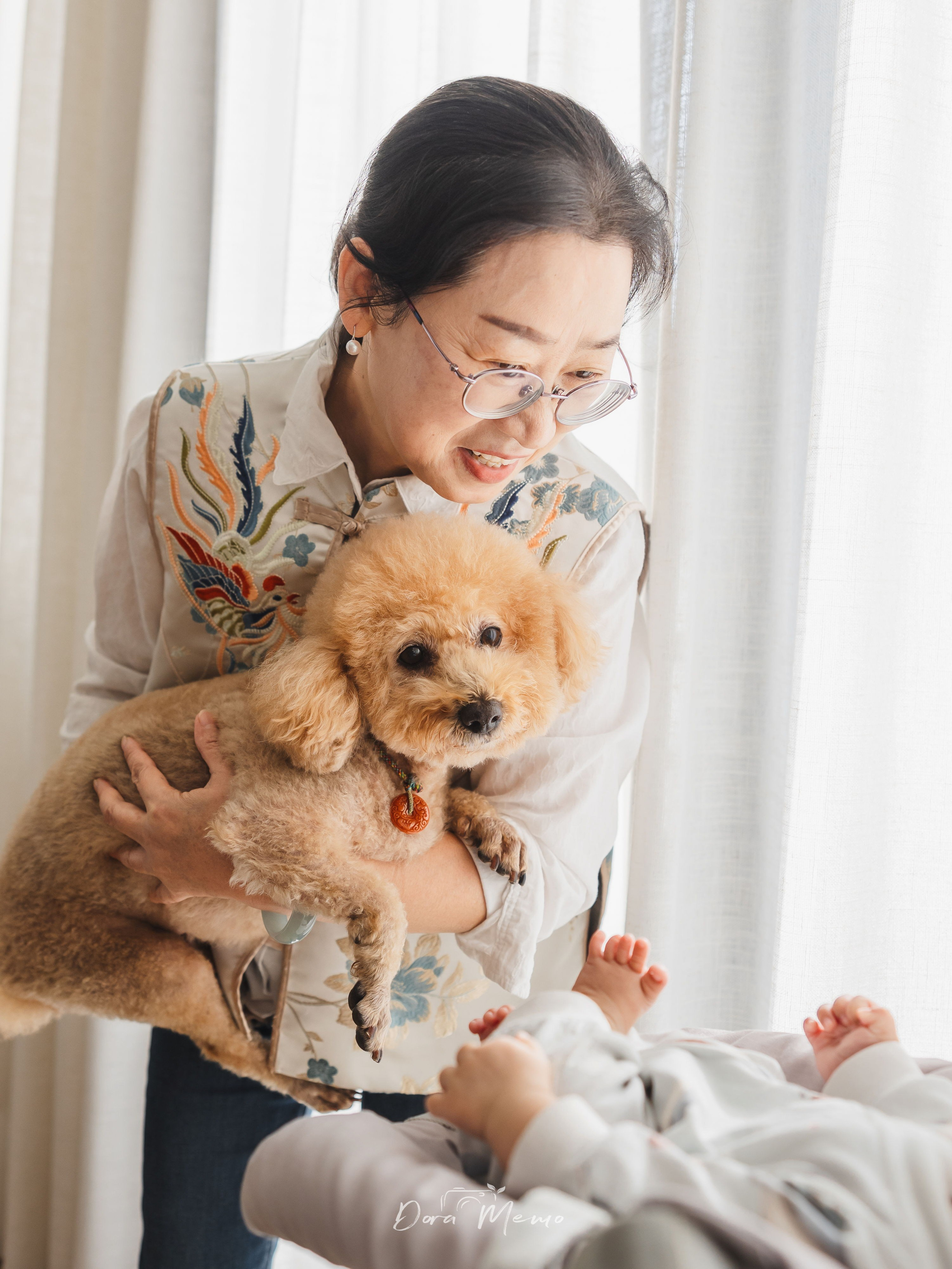 Grandmother holding the family dog while looking at a newborn baby, capturing multi-generation family life with pets in Shanghai.