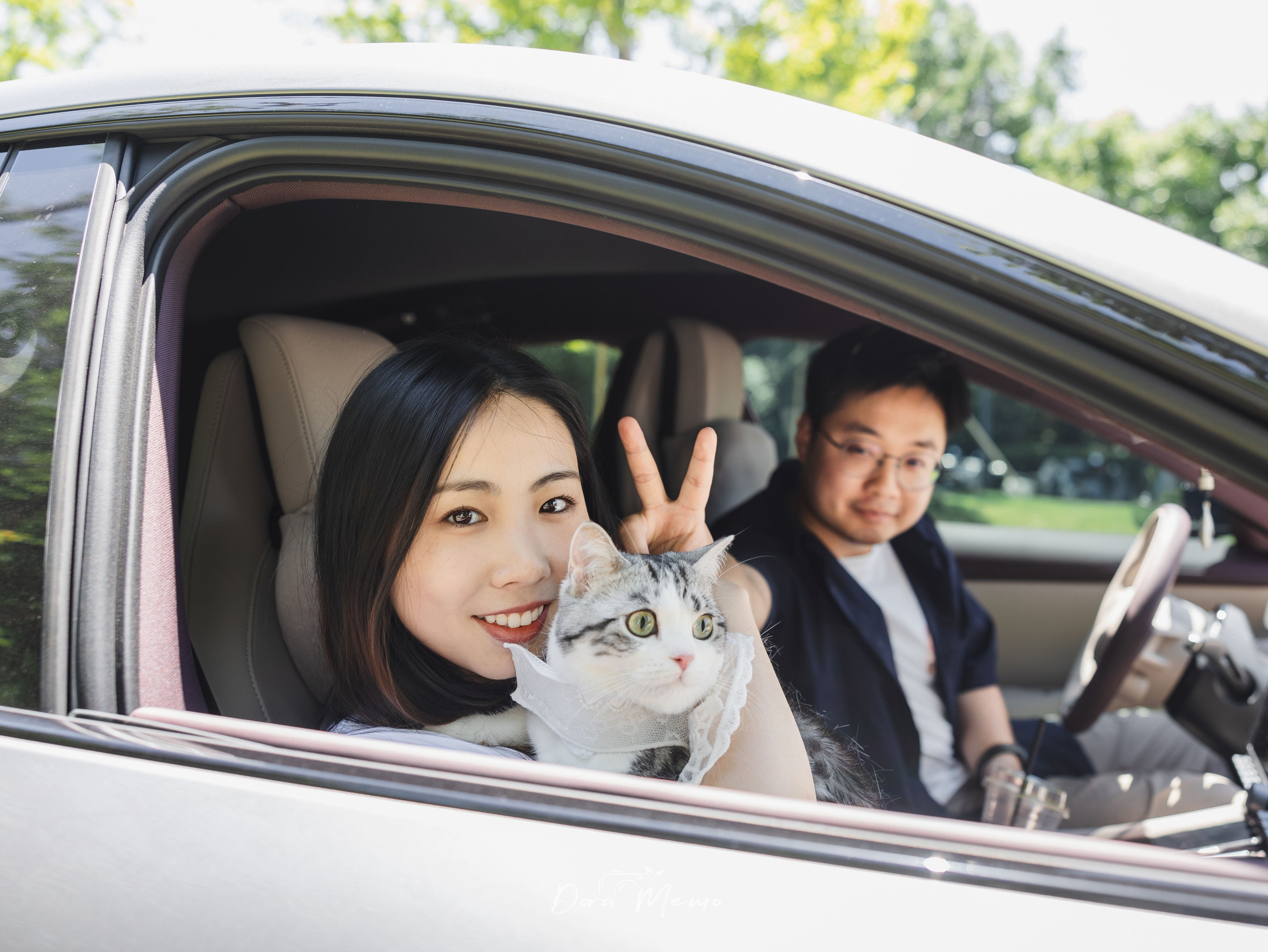 Couple in their car with their cat, woman making a peace sign, casual behind-the-scenes moment |