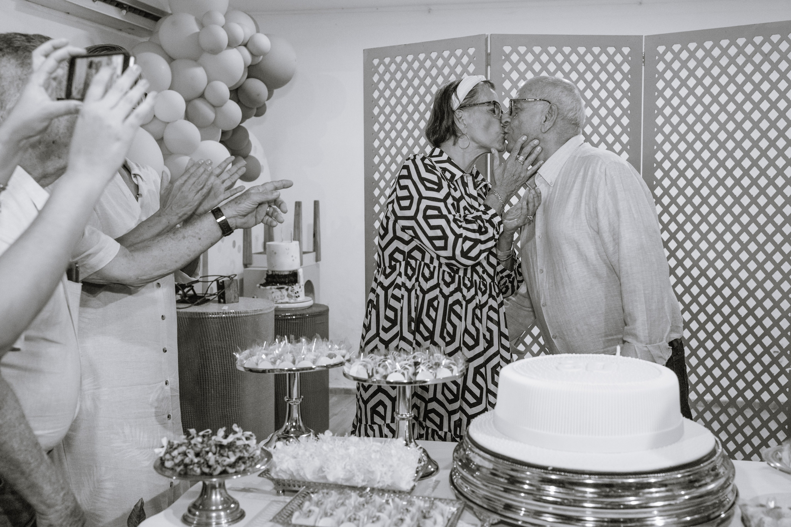 Casal comemorando aniversário de 80 anos com beijo na mesa do bolo