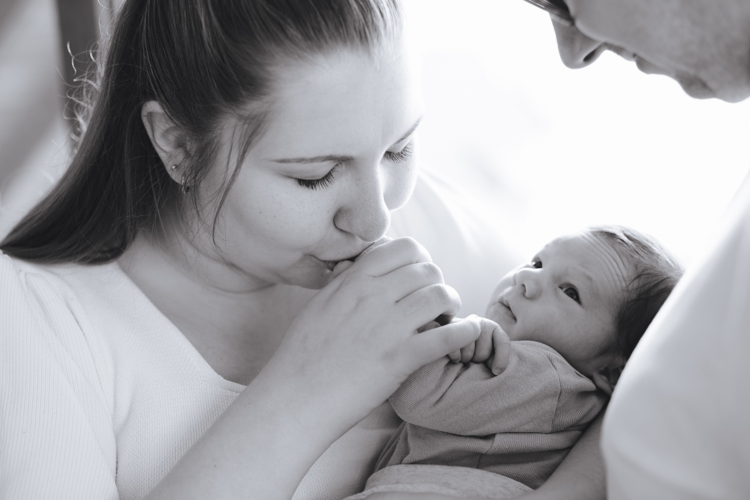 Baby in den Armen des Vaters, während die Mutter liebevoll die kleinen Händchen küsst. Ein herzlicher Familienmoment.
