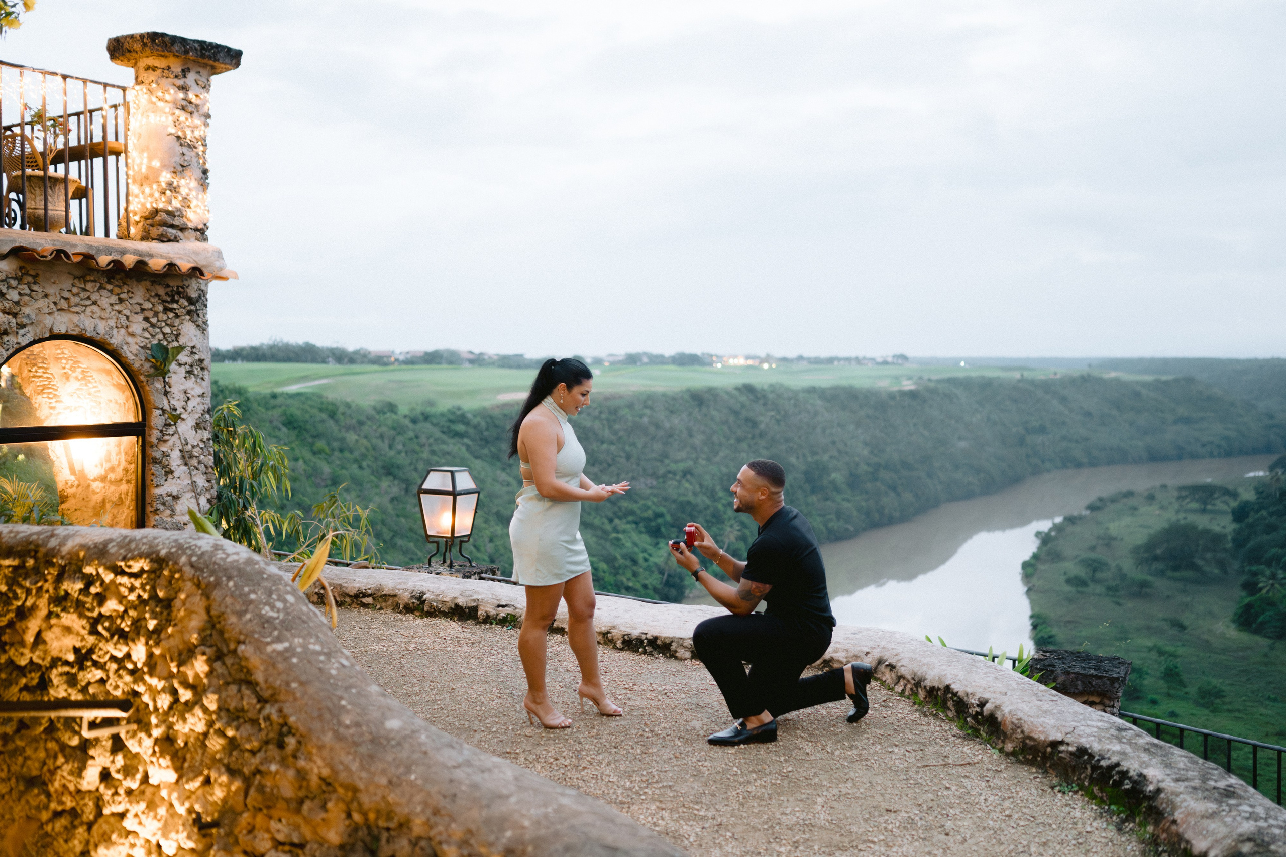 Man proposing to a woman at a scenic overlook with a river valley in the background, surrounded by rustic stone of Altos de chavon. Punta cana wedding family fashion photographer dominican republic, destination wedding photographer, elopement photography Punta Cana