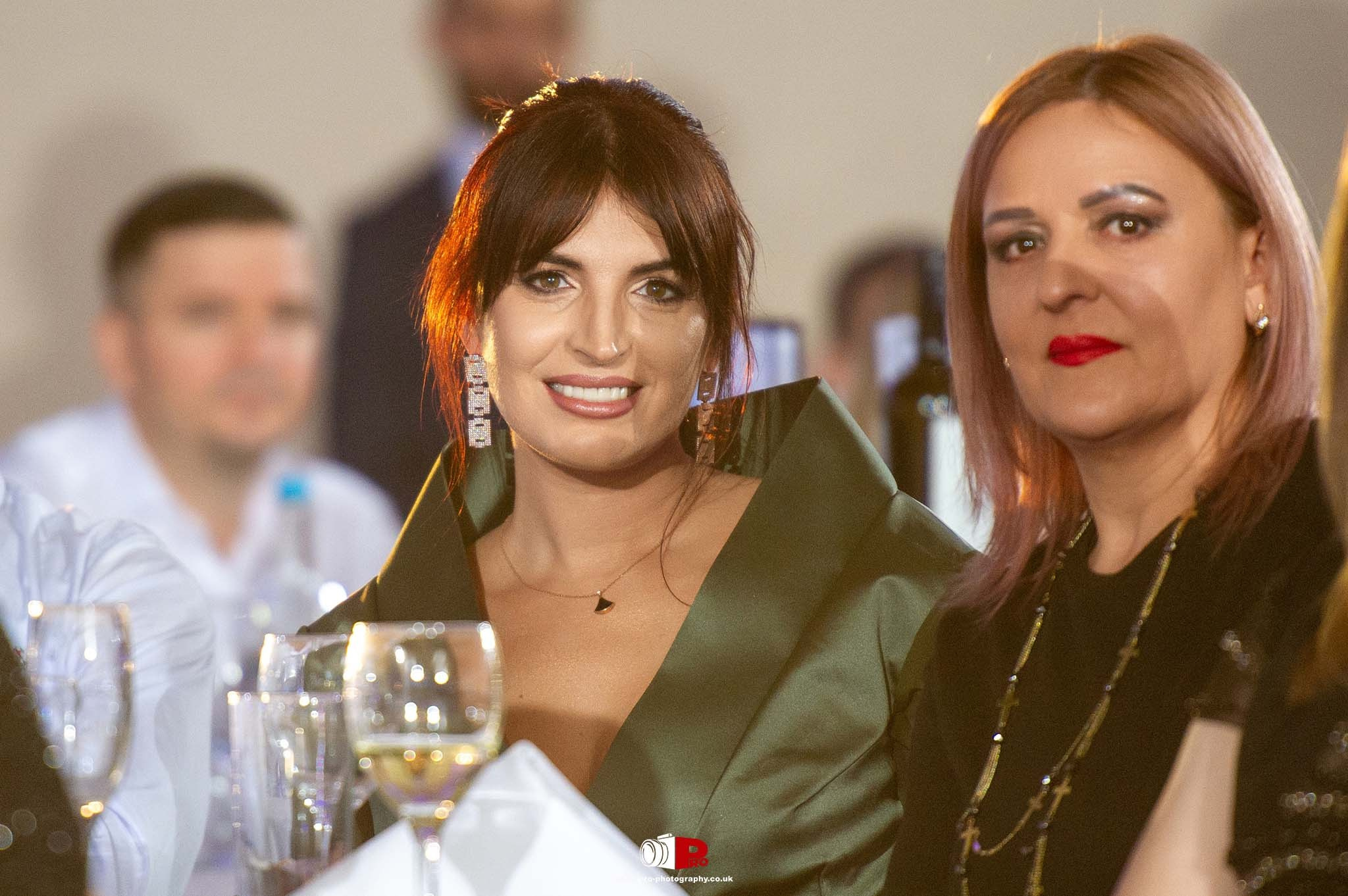 Two women elegantly dressed in green and black attire enjoying a fine dining experience at a gala event