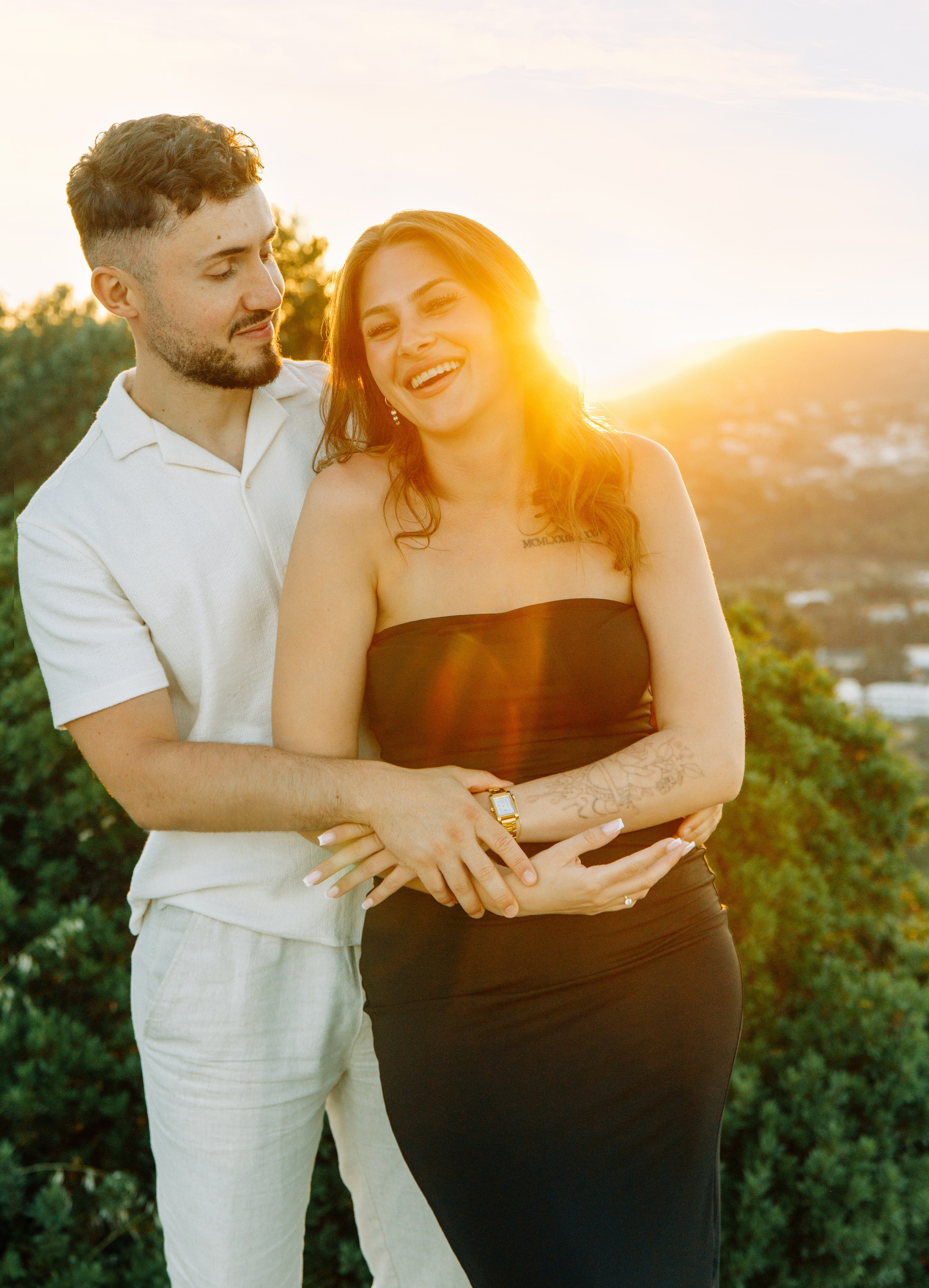 "Liebevoller Blickkontakt: Ein Paar auf dem Felsplateau des Profitis Ilias vor der Kulisse von Faliraki und dem Mittelmeer."