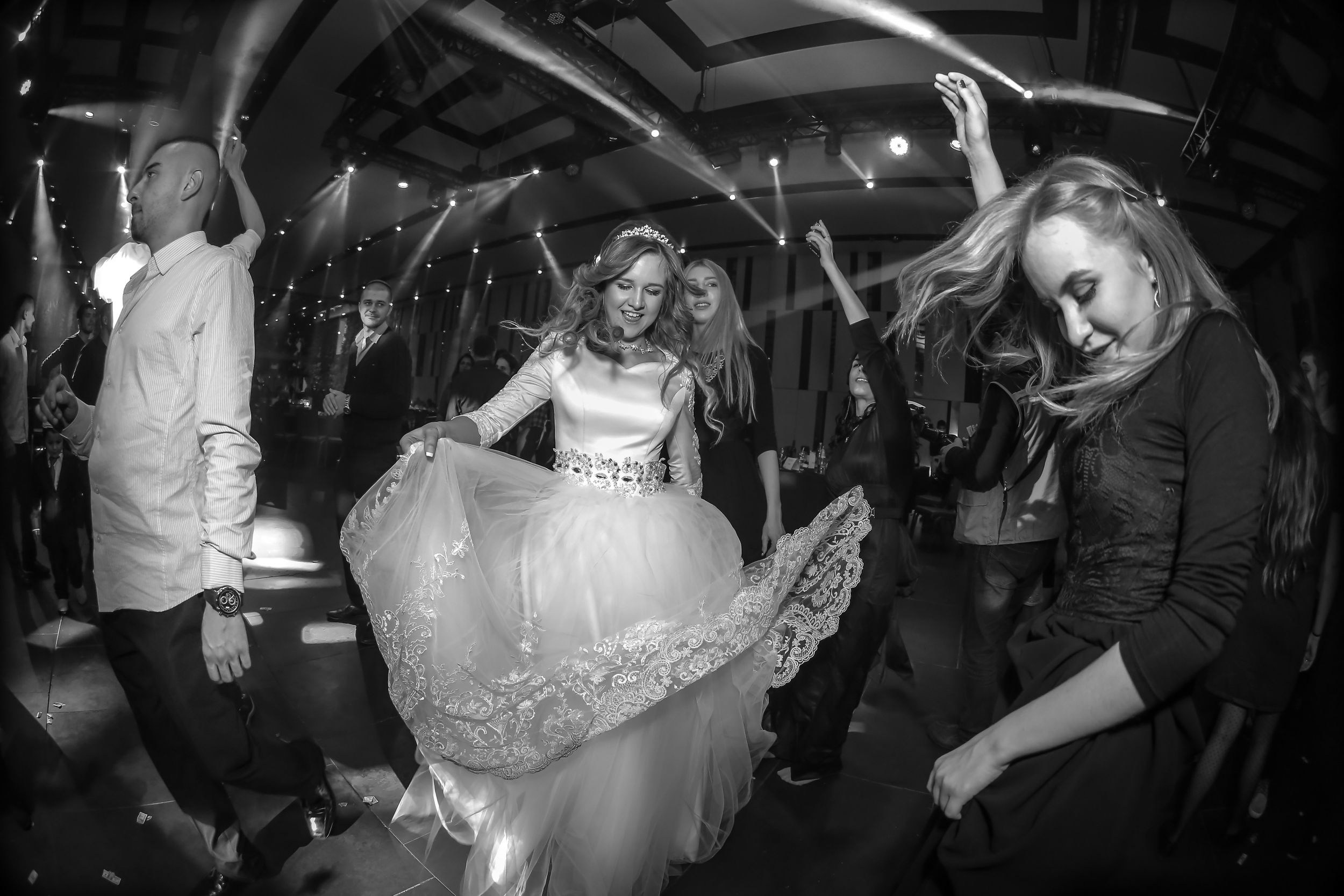 Bride dancing joyfully at a wedding reception, surrounded by guests celebrating. Candid black and white documentary wedding photography capturing real emotions and movement