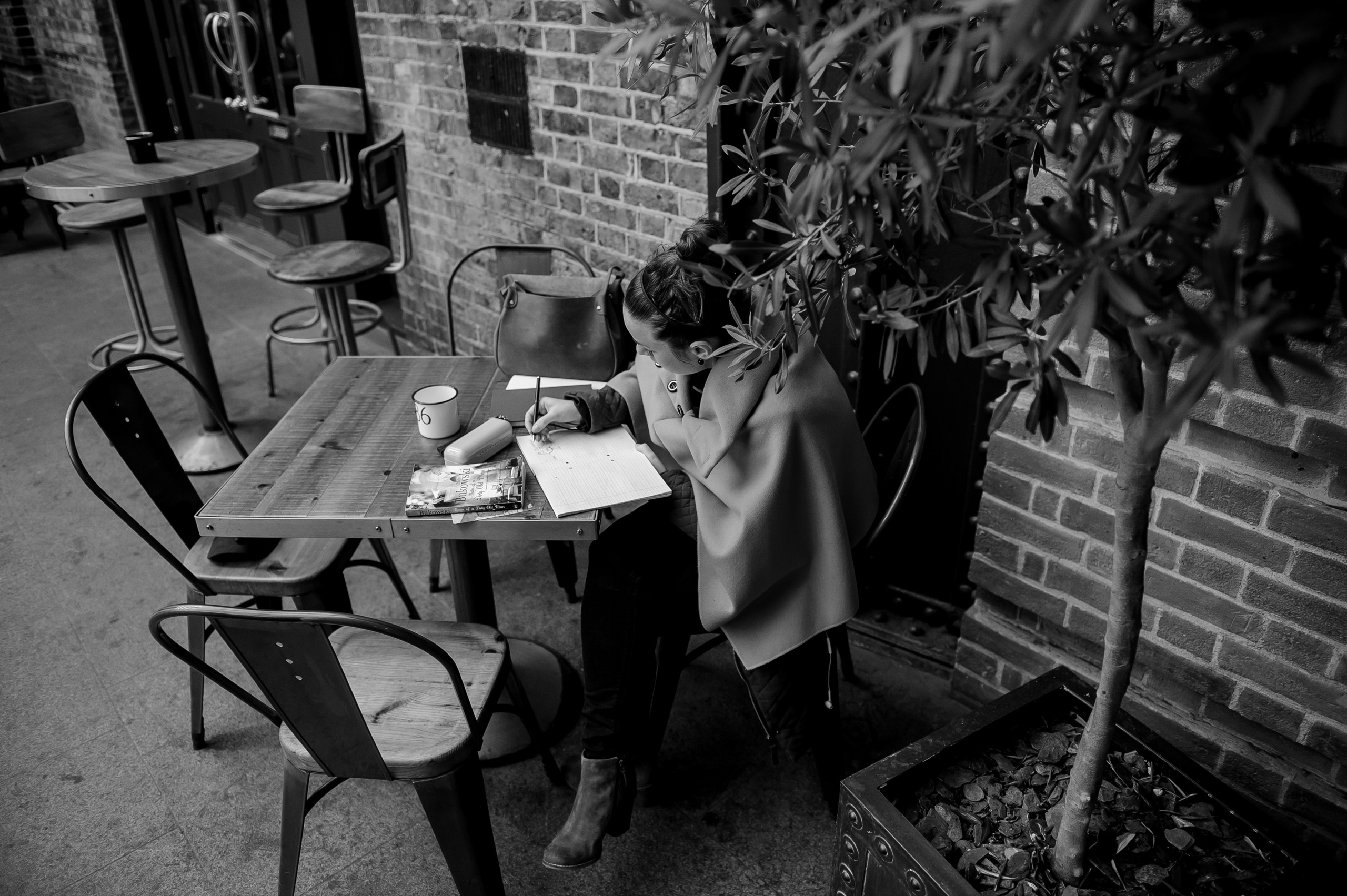 A girl is sitting at a table on the terrace, taking notes in a notebook.