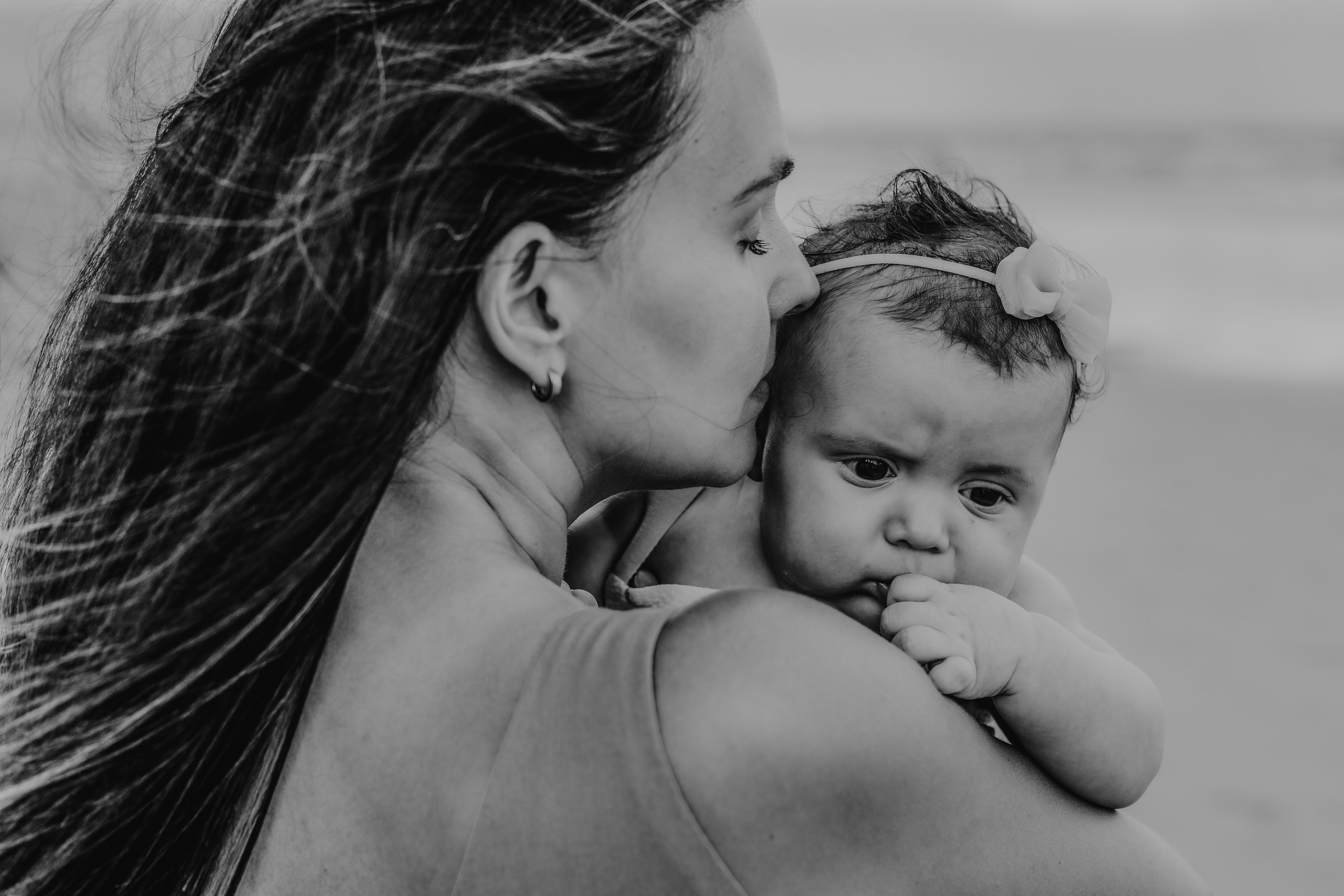 Mãe beijando a filha bebê na praia em momento intimista