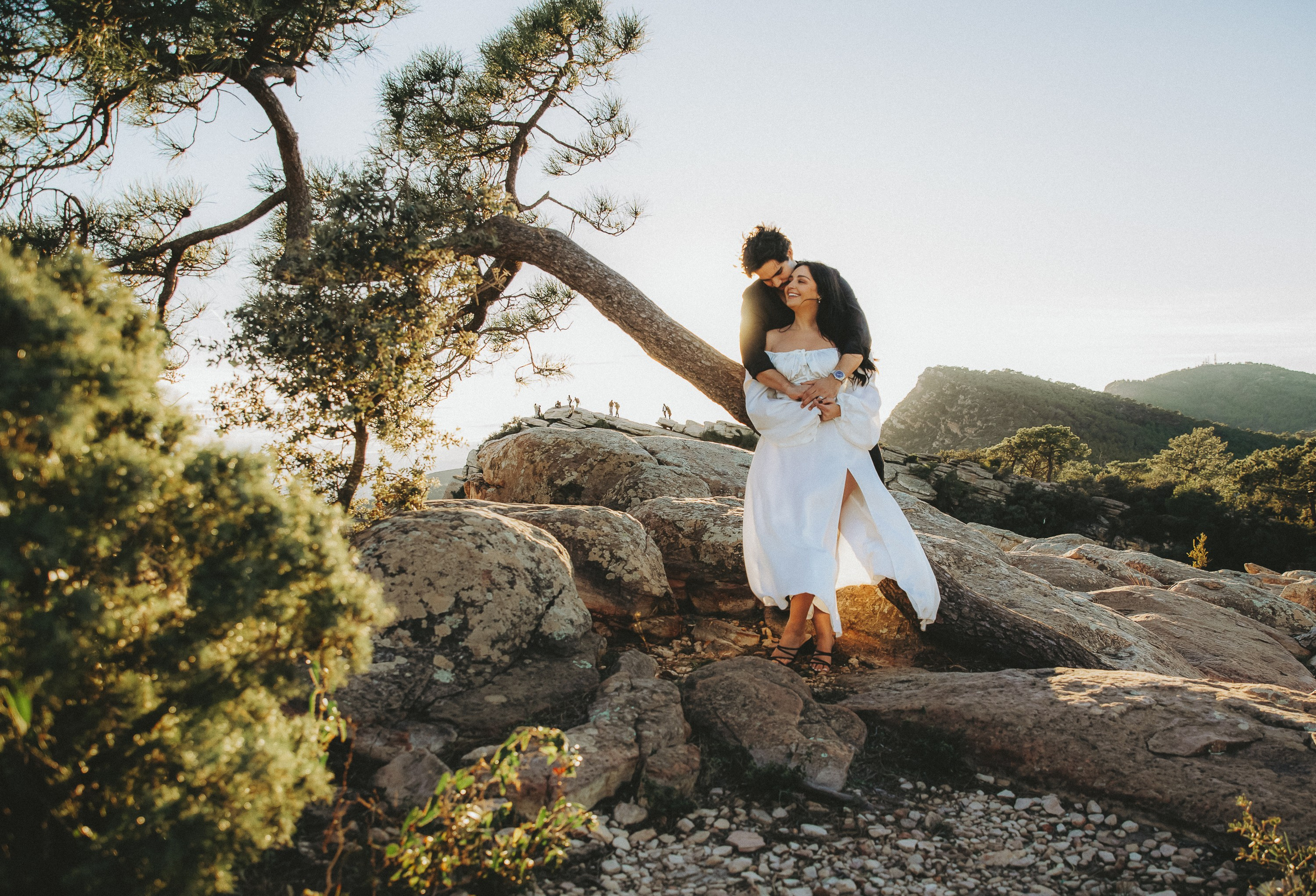 Bride standing on natural rock formations surrounded by trees during a sunset destination wedding in Barcelona, Spain. This artistic elopement portrait reflects the elegance and adventure of an intimate mountain ceremony.