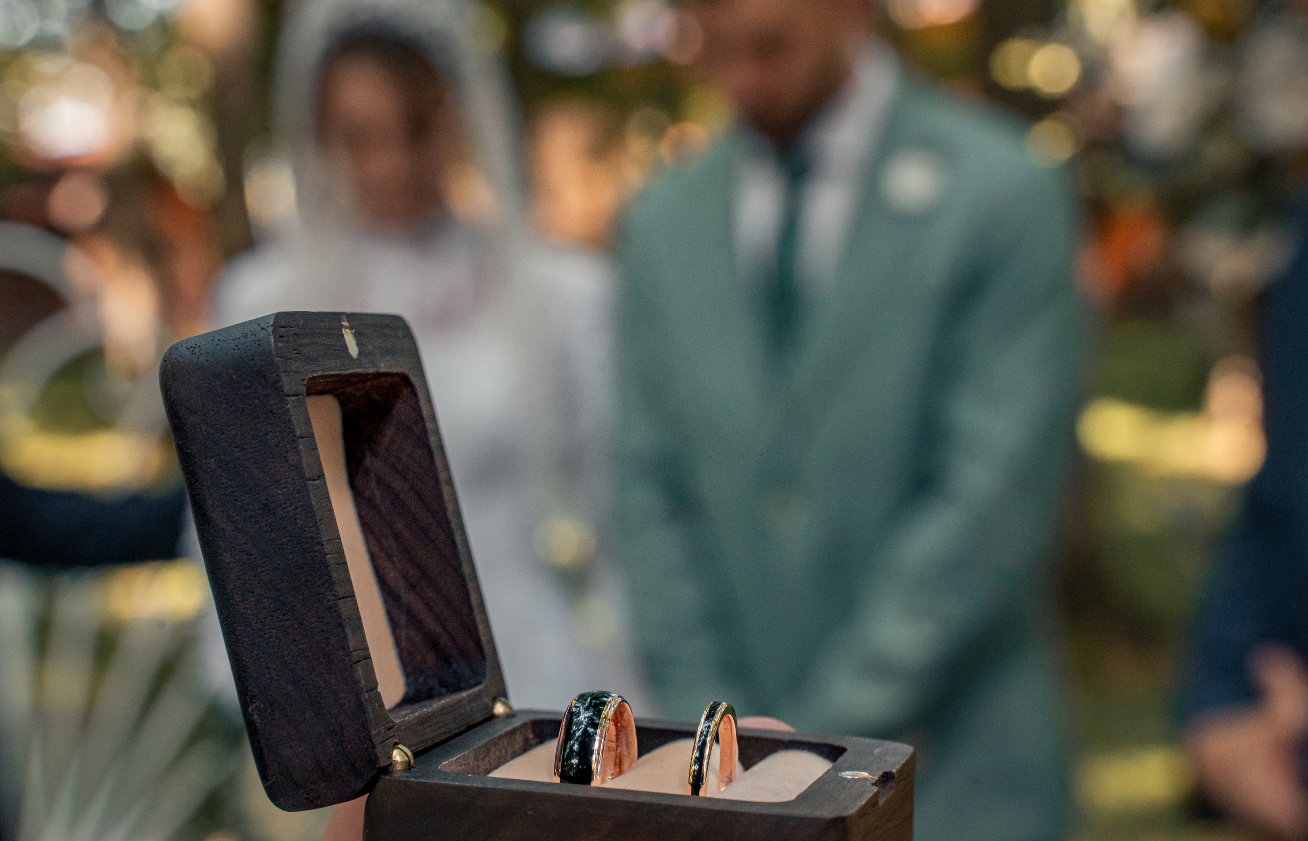 Verighete de nuntă în cutie de lemn, miri în fundal defocalizat, fotografie detalii nuntă, incadru.ro.