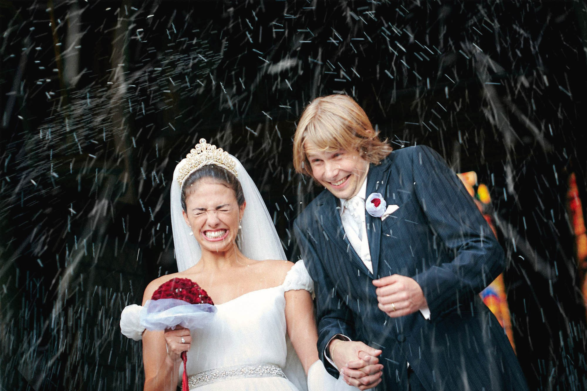 Brazilian bride and Czech groom laughing as they're showered with rice and rose petals leaving St. Ludmila's Cathedral.