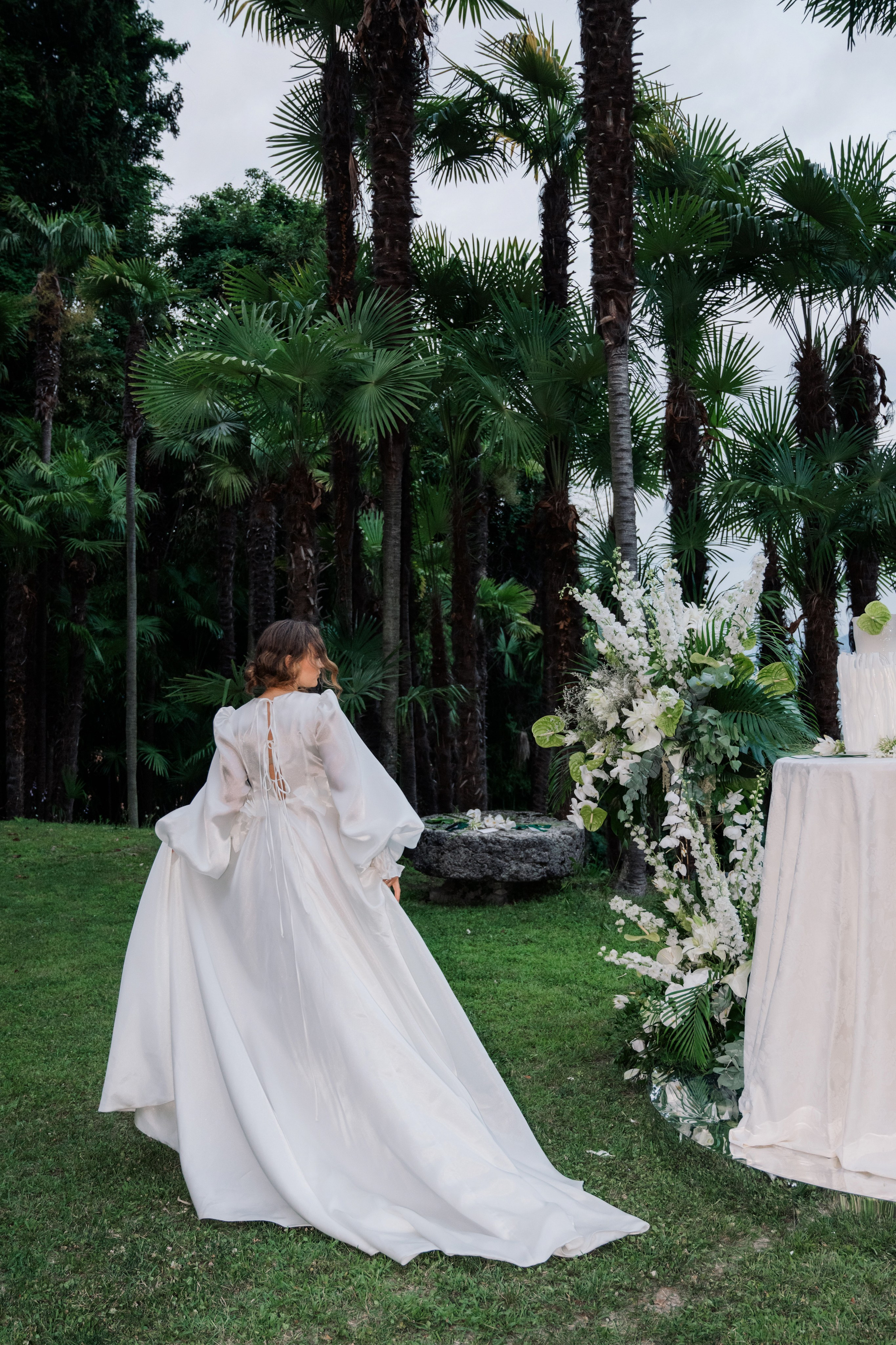 a woman in a wedding dress is standing next to a table with a flower arrangement