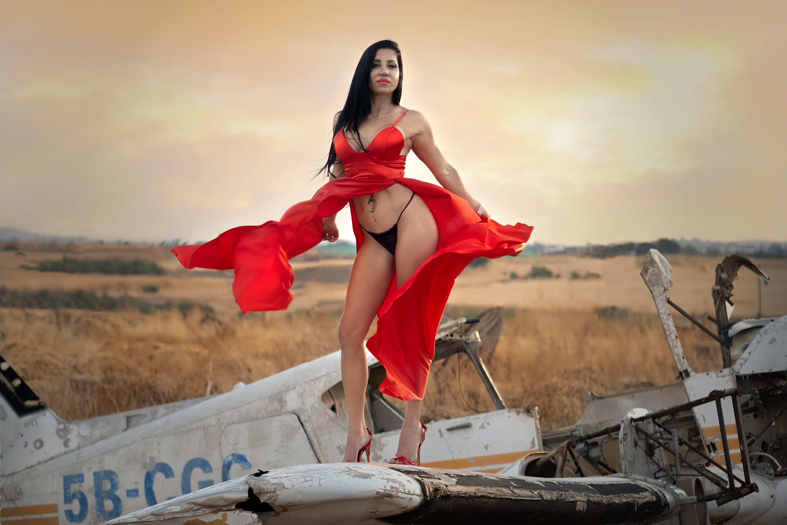 Lady in red dress standing on wreck plane at sunset