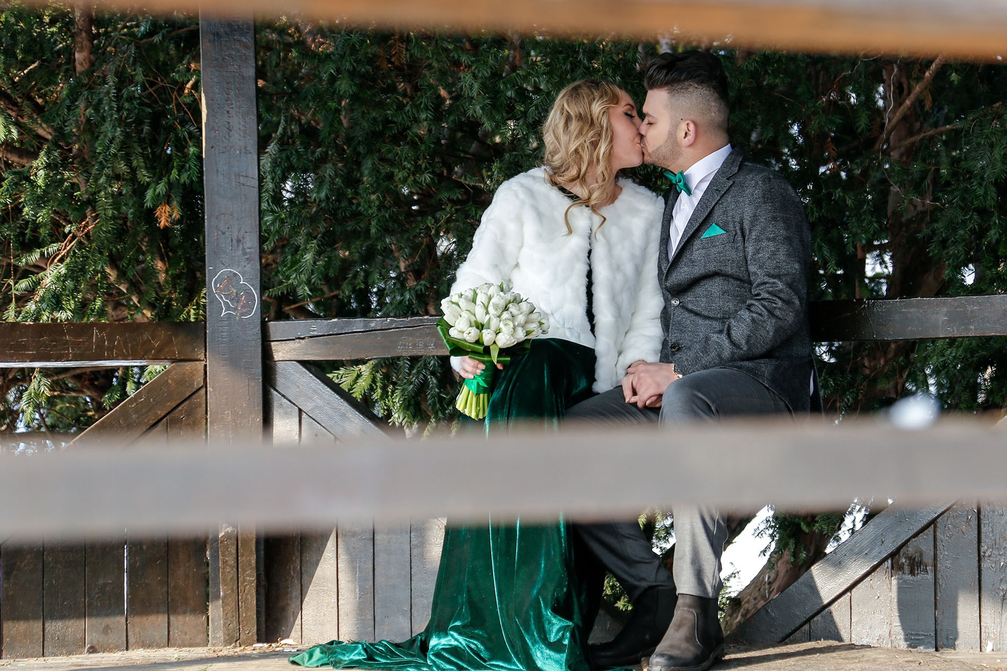 Romantic kiss between the newlyweds sheltered inside the wooden gazebo, a passionate moment in the middle of the winter setting.