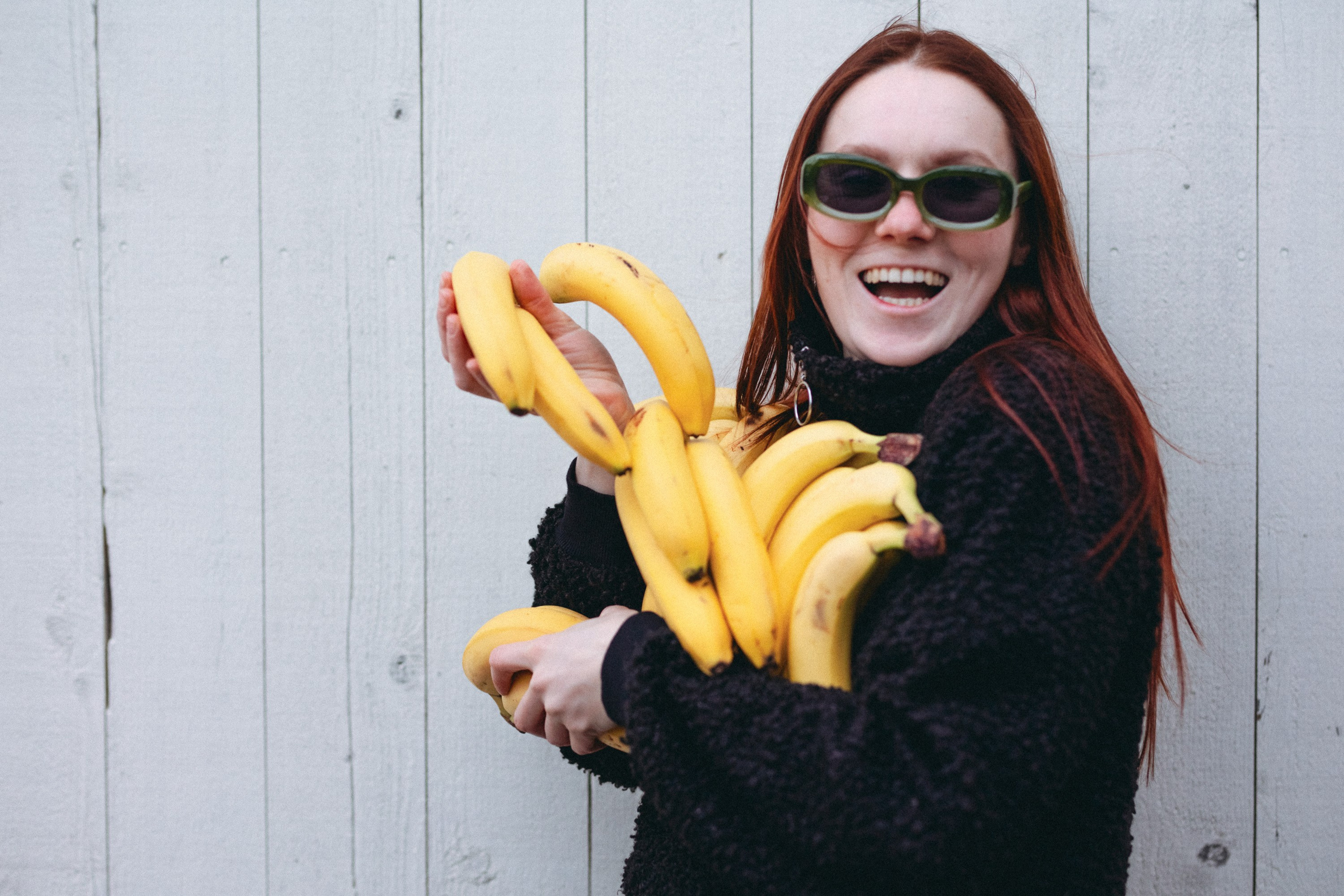 Hymyilevä tyttö pitää keltaisia banaaneja sylissä