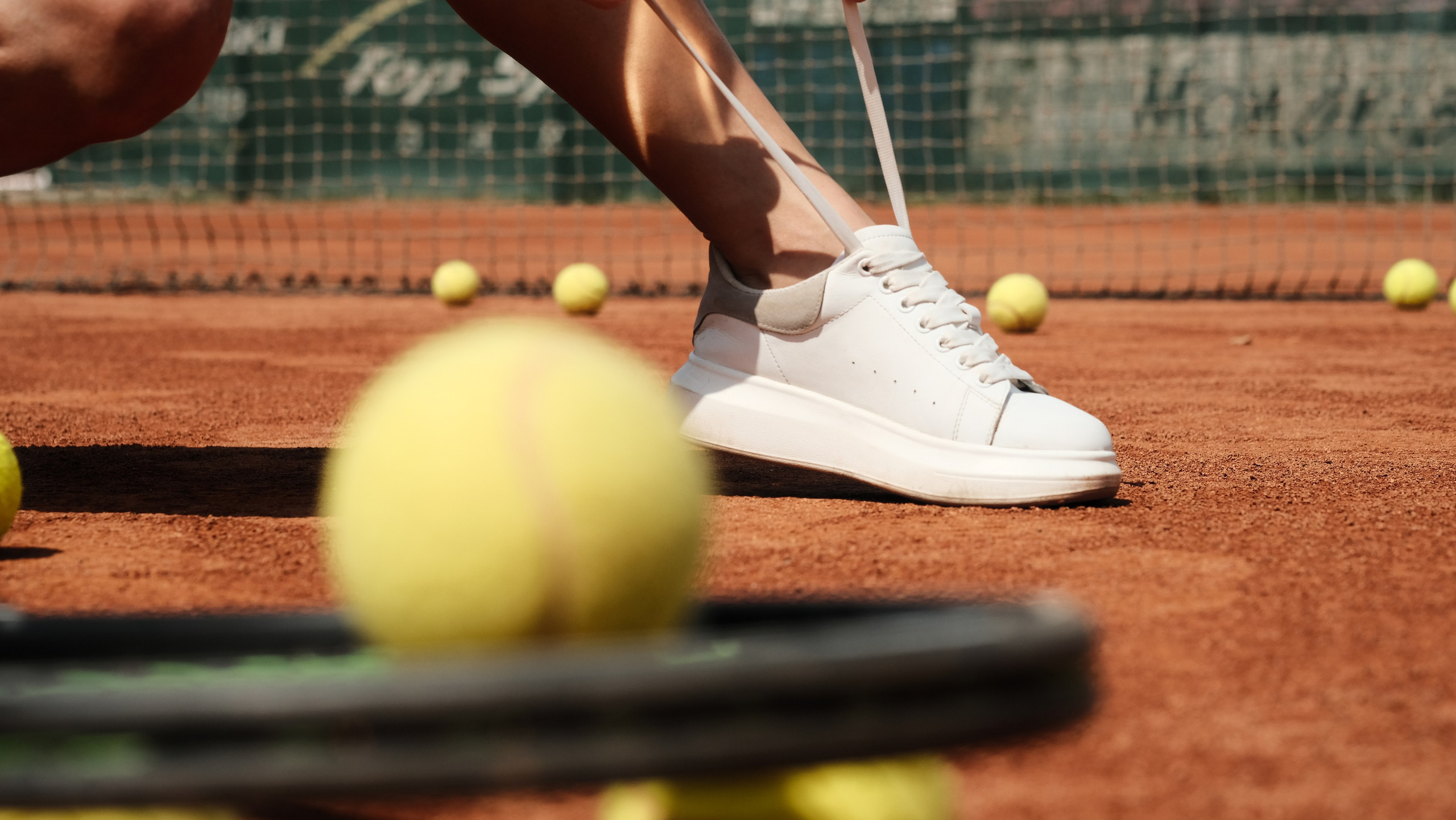 девушка завязывает шнурки на кроссовке перед игрой в теннис