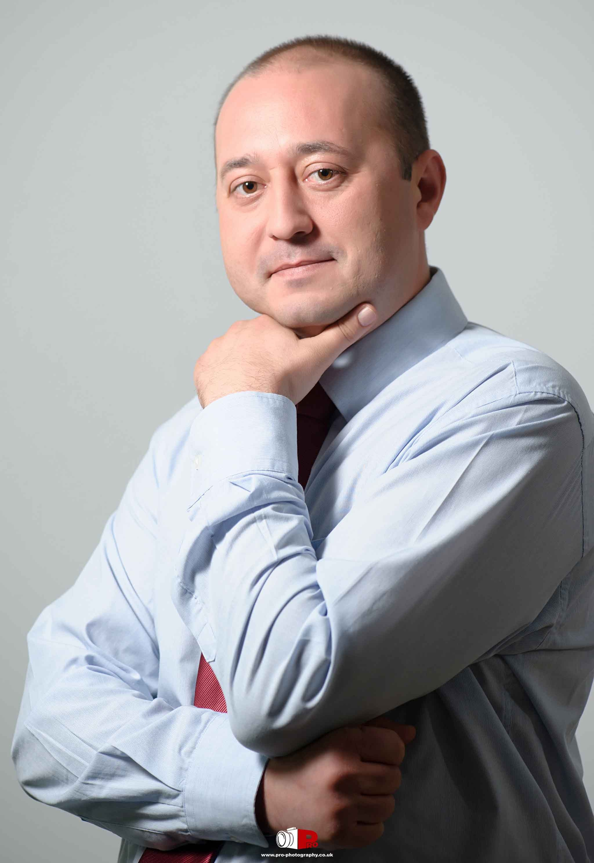 Man posing confidently in a light blue shirt and red tie, resting his chin on his hand.
