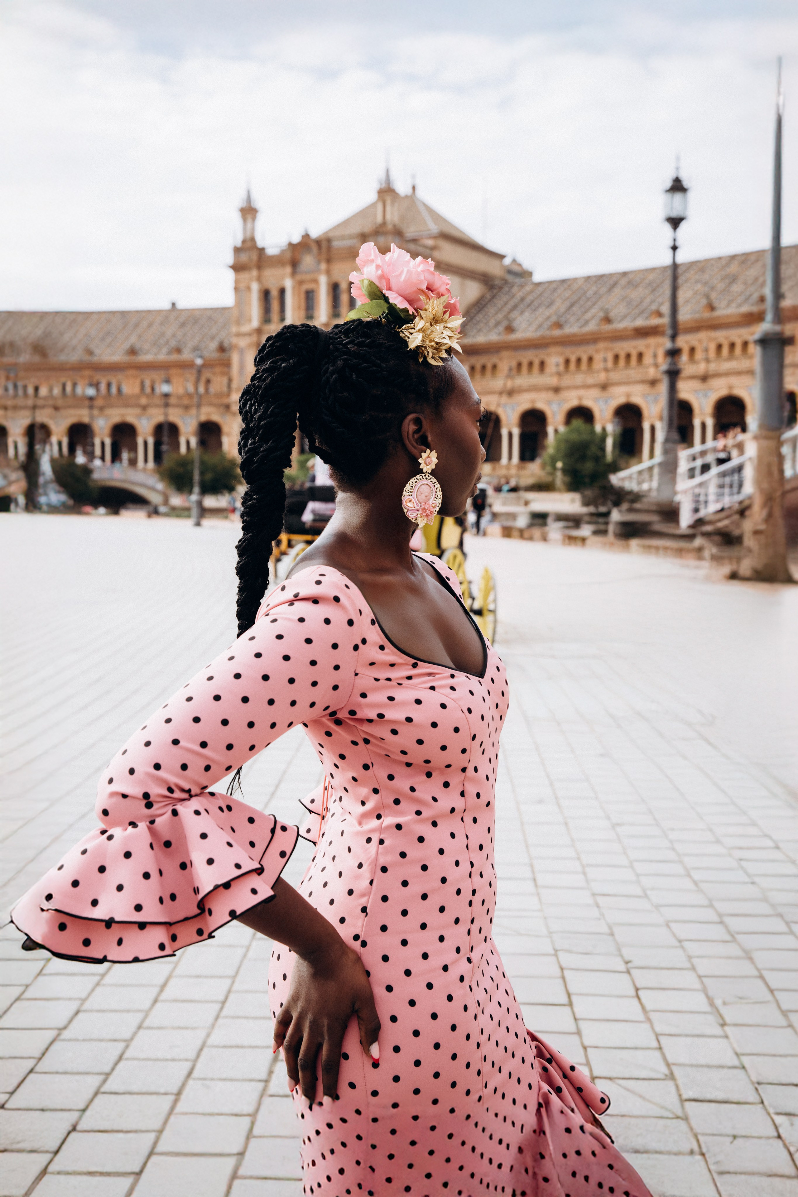 Элегантная женщина в традиционном платье фламенко с цветами в волосах позирует на площади Испании в Севилье, Испания — яркий культурный портрет, идеально подходит для тех, кто ищет художественную и аутентичную портретную фотосессию в Севилье и южной Испании.