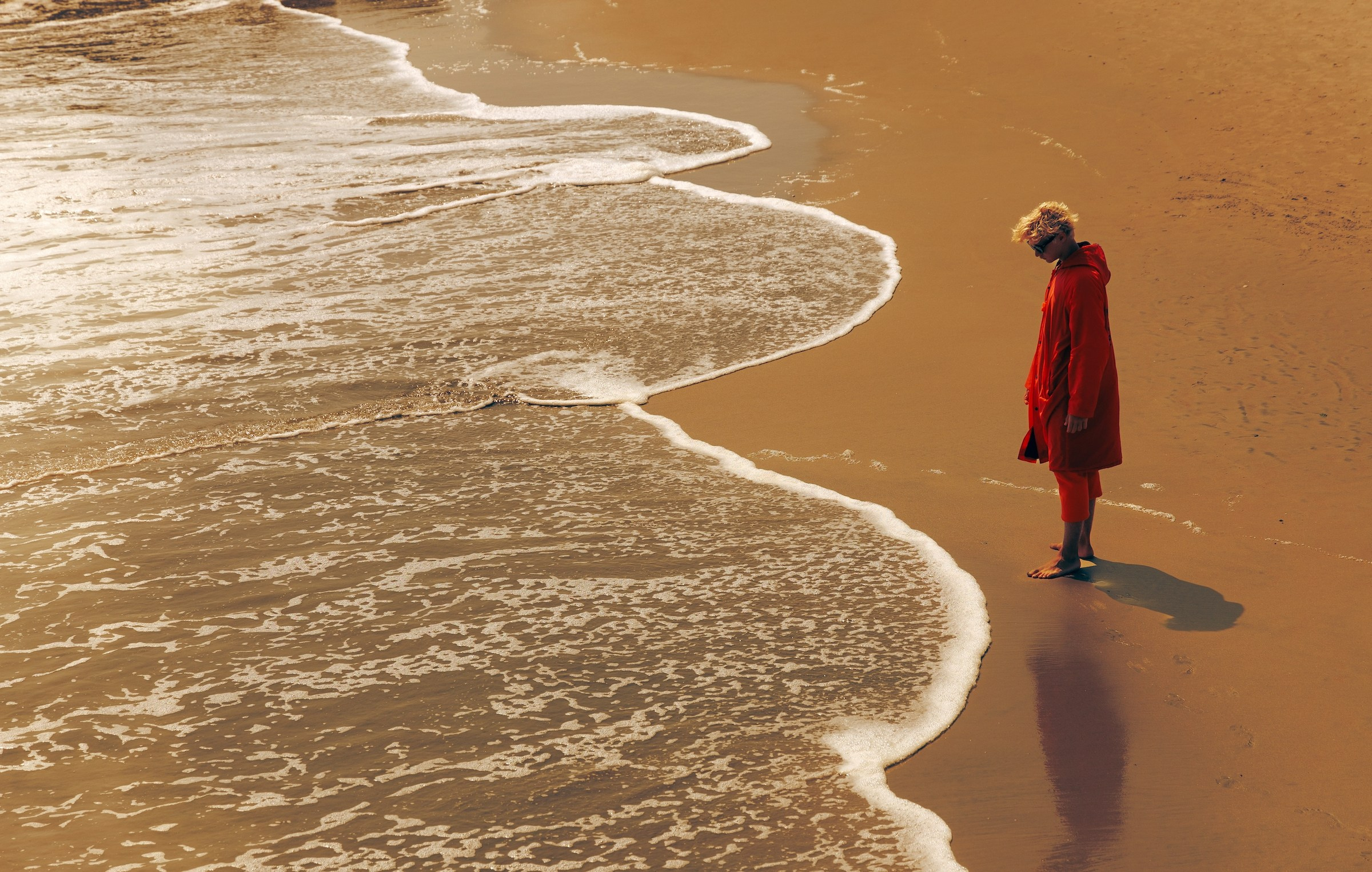 “The last lifeguard”, is a photographic series exploring a solitary figure walking the coastline during low tide. The beach is nearly empty, the water has withdrawn, and the lifeguard — dressed in a red coat — becomes a small yet powerful symbol of human presence within a vast natural space.I am drawn to the tension between responsibility and isolation. A lifeguard is someone whose purpose is to protect others, even when there is no one left on the shore. Walking along an empty beach, the figure becomes a quiet witness, a guardian without an audience.By photographing from above and from a distance, I reduce the human form to a moving mark between sand and sea. The coastline becomes a stage for silence, memory, and observation. These images are not tied to a specific location; they reflect an emotional state — the moment when the world feels both beautiful and emptied, and one person carries the meaning of being there. Denis Bold / Photographer (New York/USA)