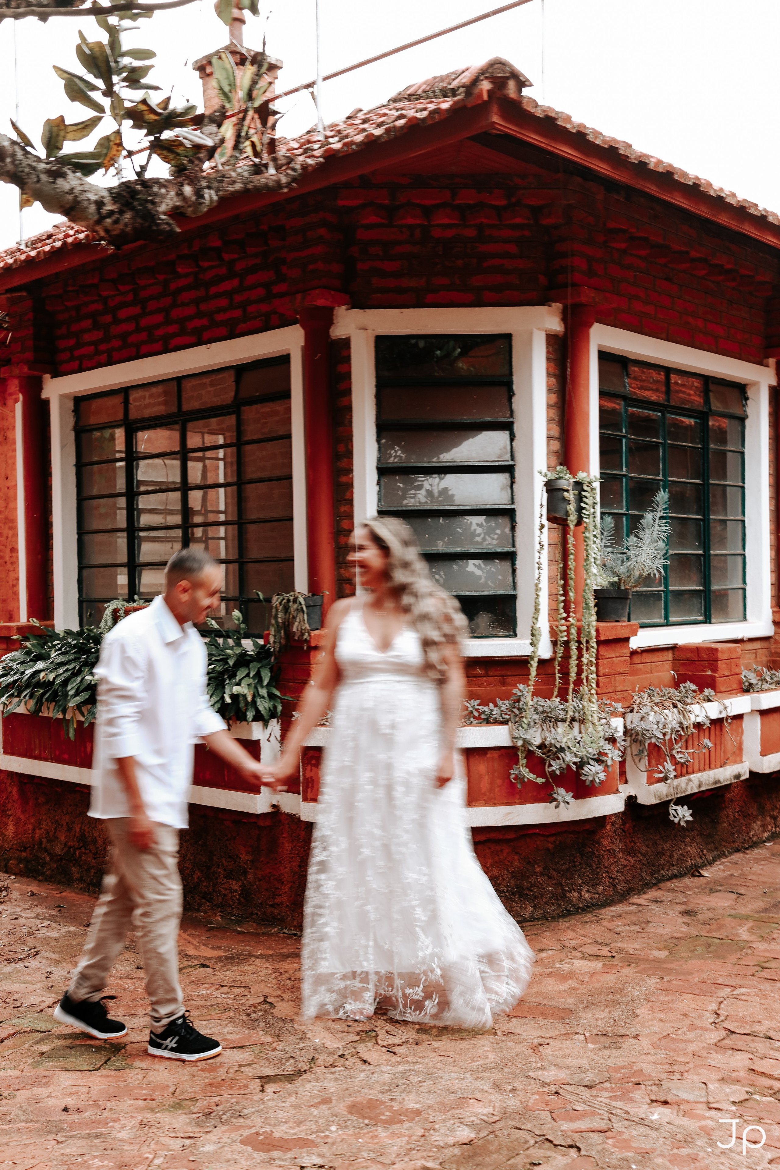 Ensaio de casal em Pederneiras com casal caminhando de mãos dadas em frente à casinha de madeira vermelha.