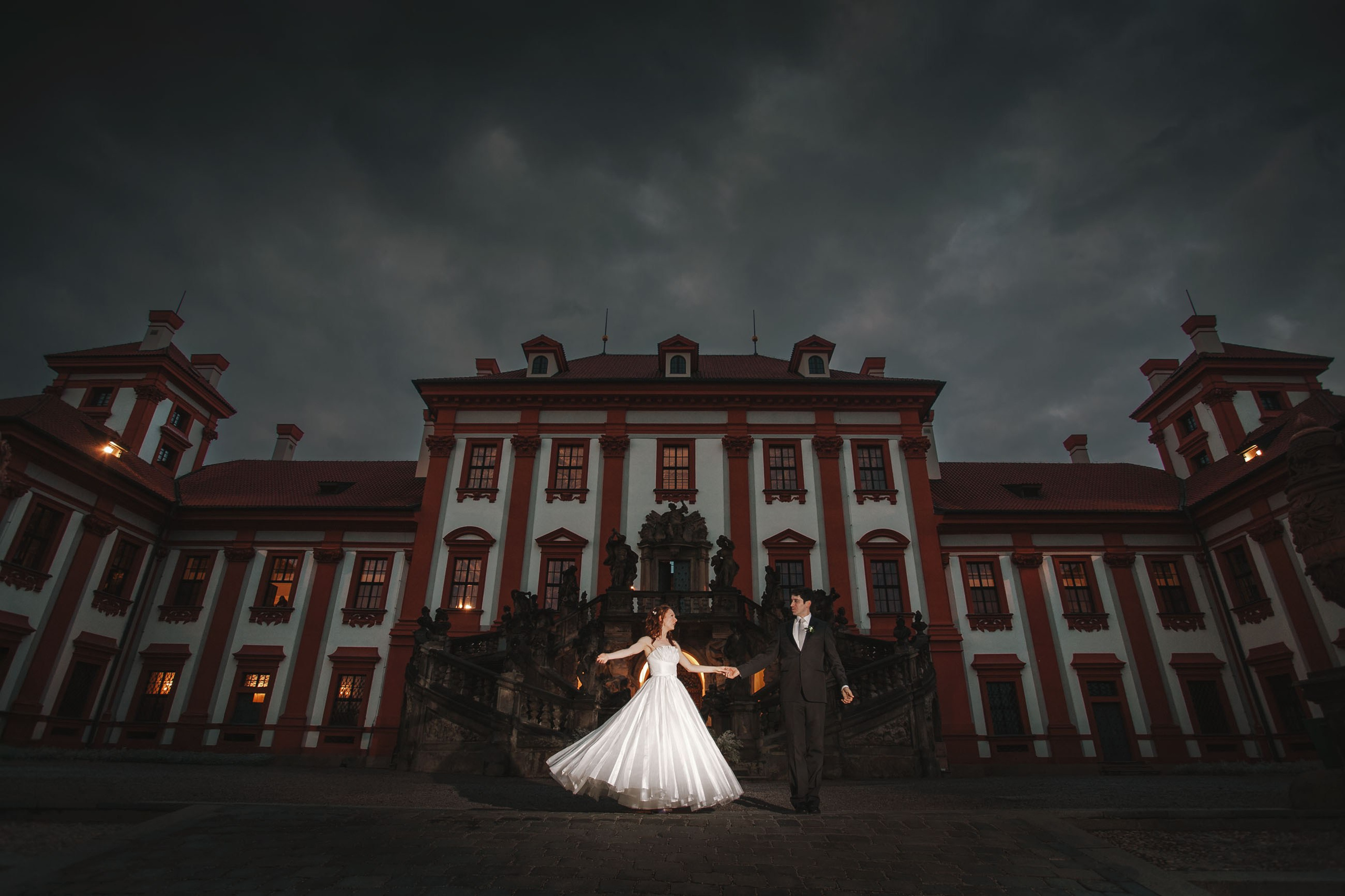 American groom and Russian bride practicing first dance at night at Troja Chateau, Prague