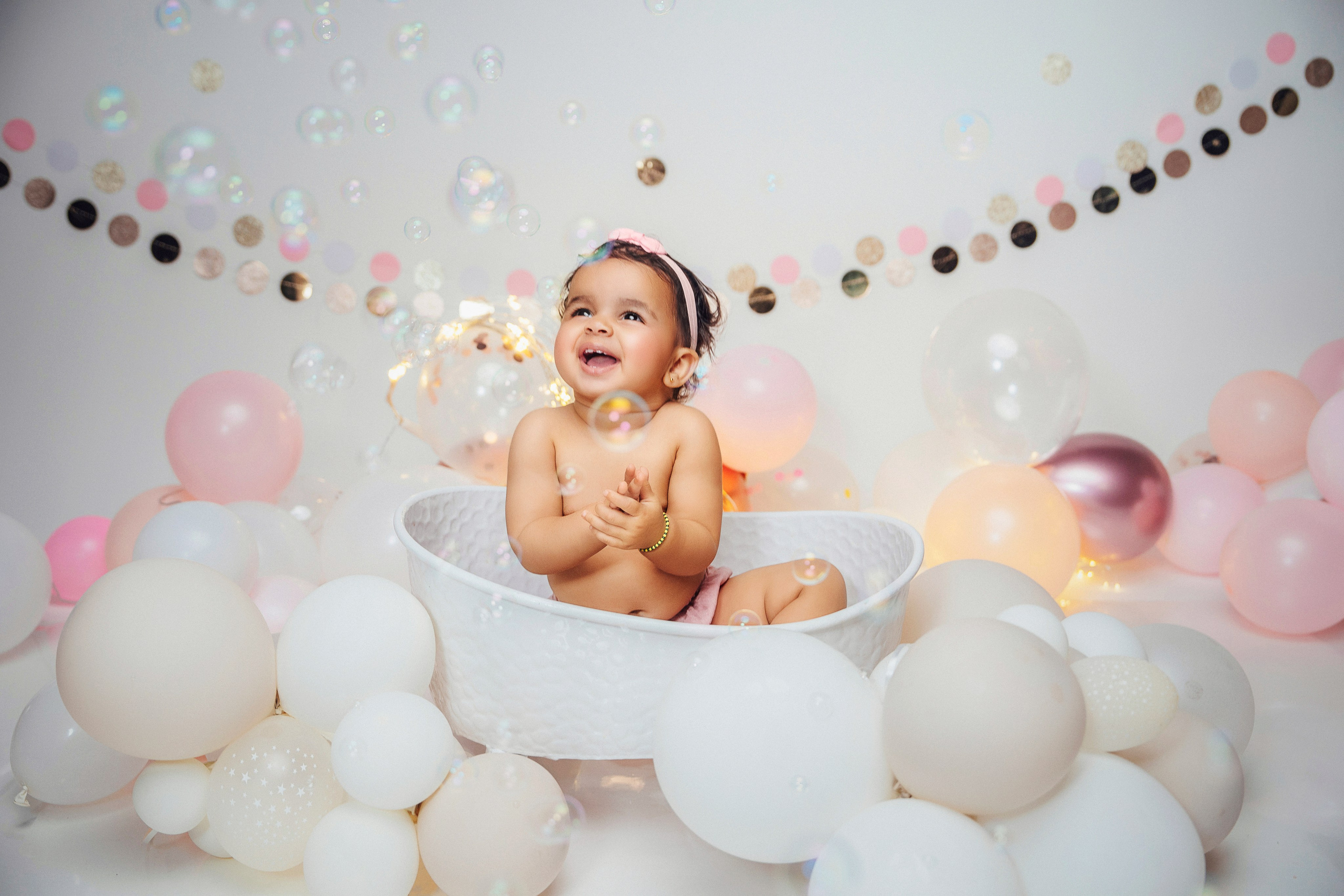 Годовалая девочка наслаждается купанием в ванночке с шарами — нежная и светлая фотосессия.