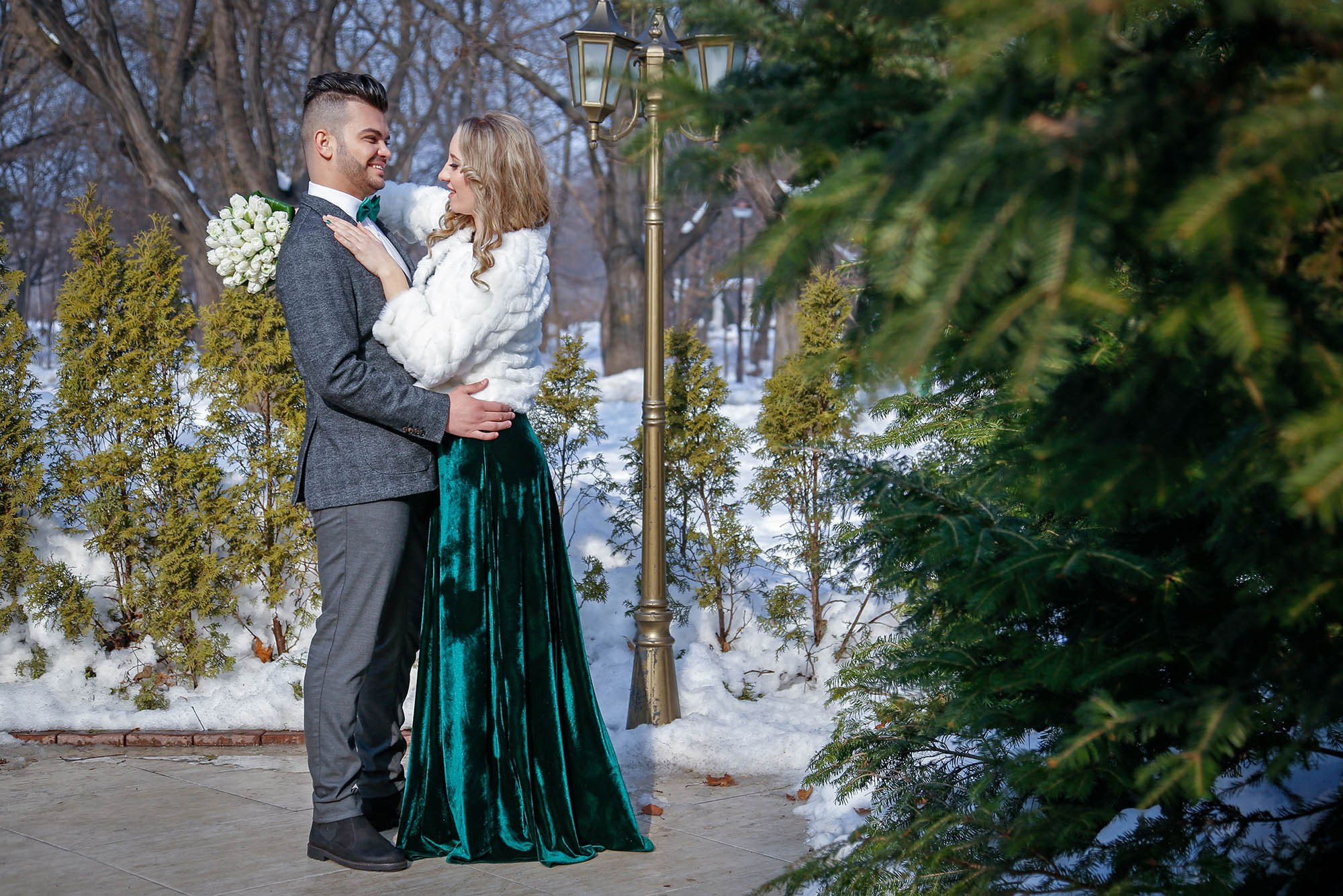 Wide artistic shot of the newlyweds walking down a snowy pathway in a Bucharest park, capturing the authentic winter wedding atmosphere.