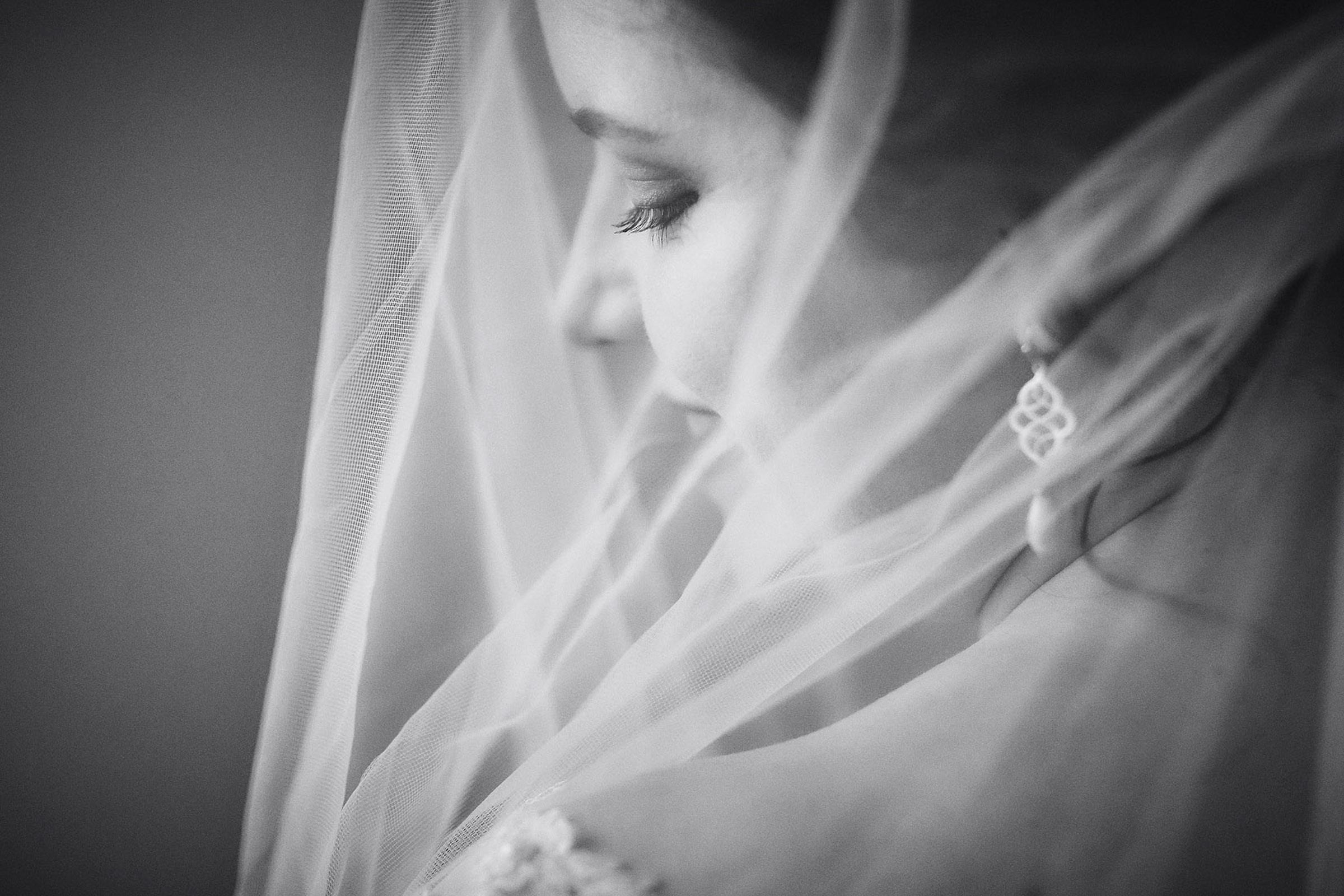 A tight shot of a smiling bride's face is seen behing a veil in this monochrome image.
