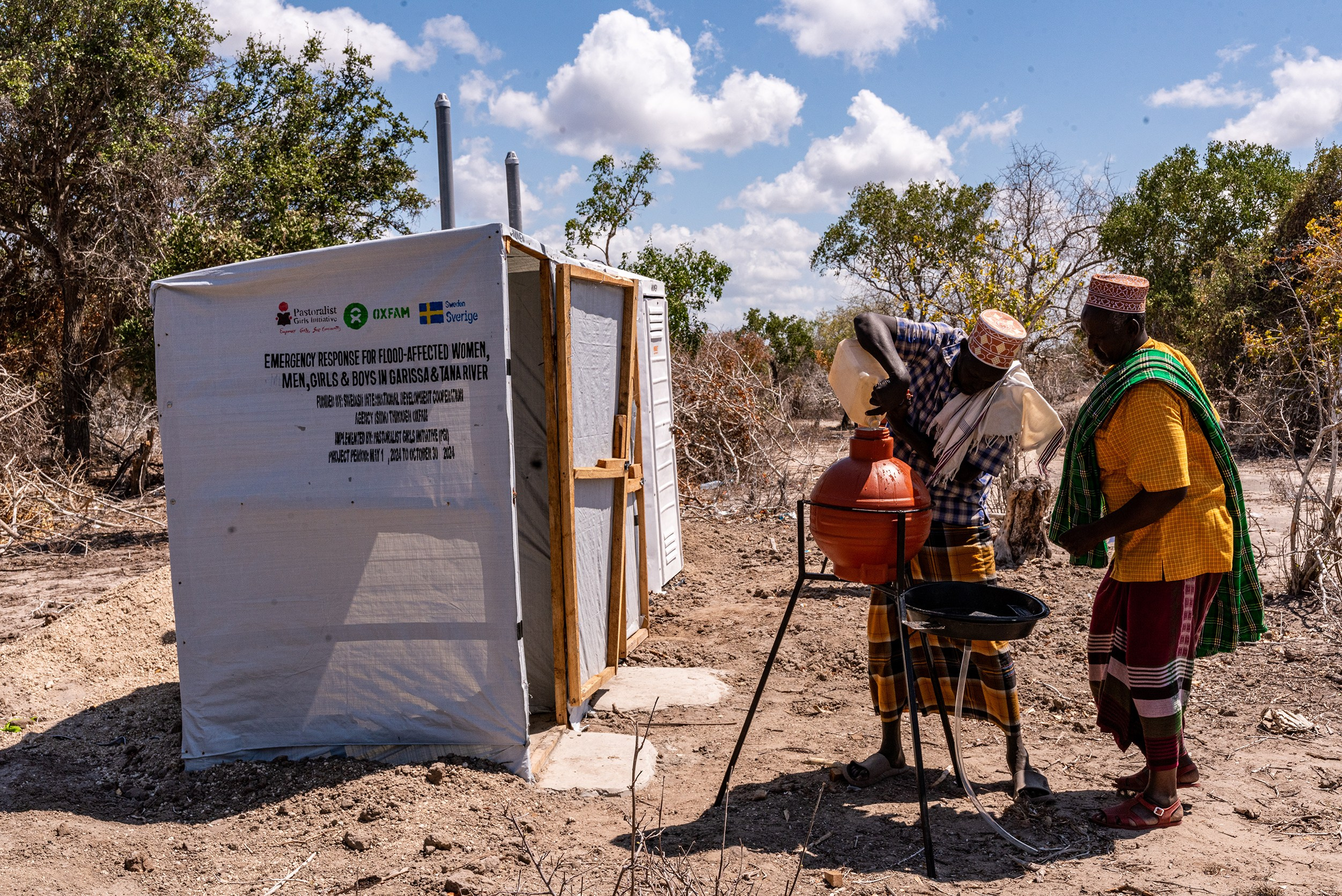 A wide-shot of two men washing their hands next to a line of mobile toilets, in Garissa county. Documentary storytelling.