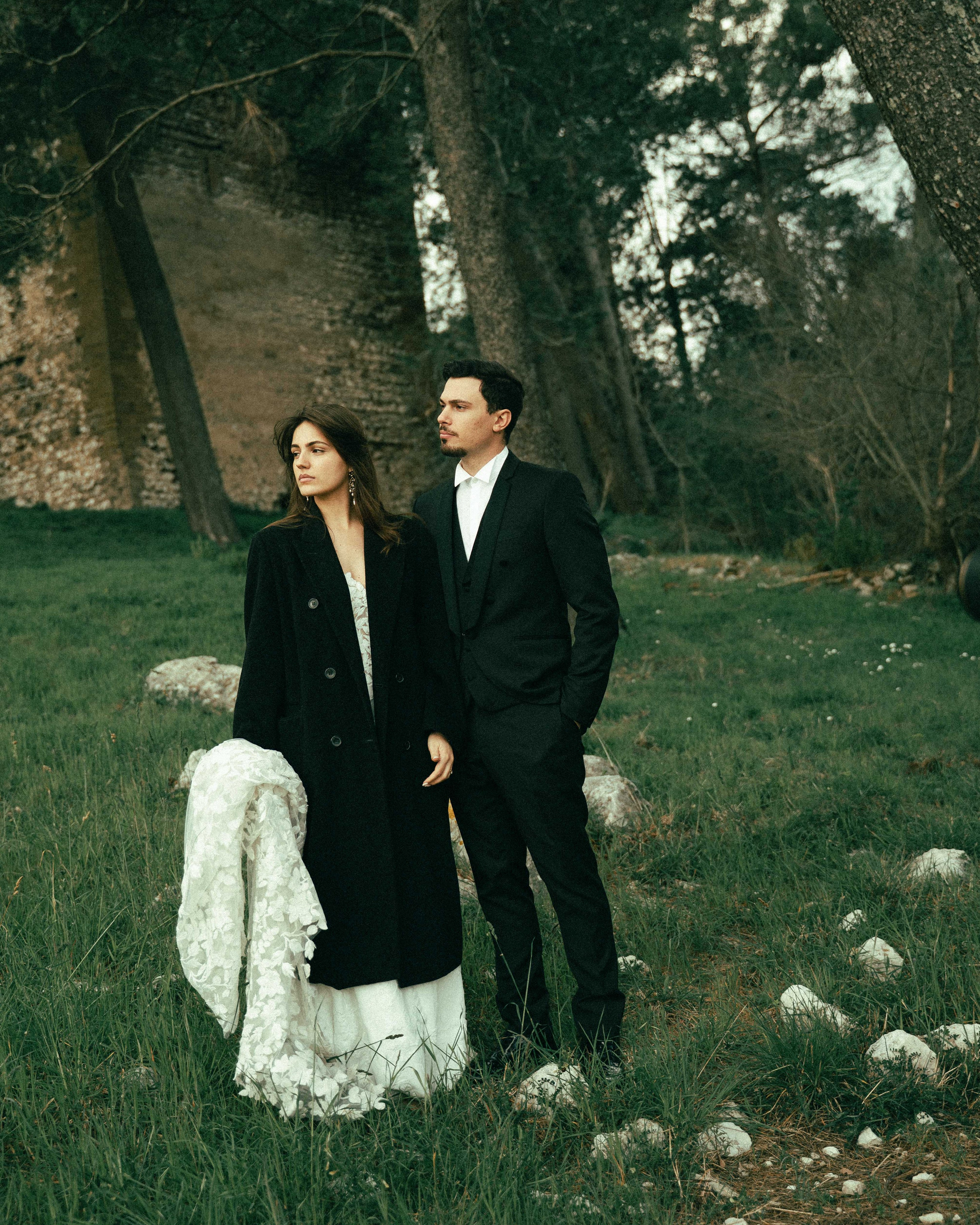 Bride and groom together in a forest, bride wearing a coat over her wedding dress