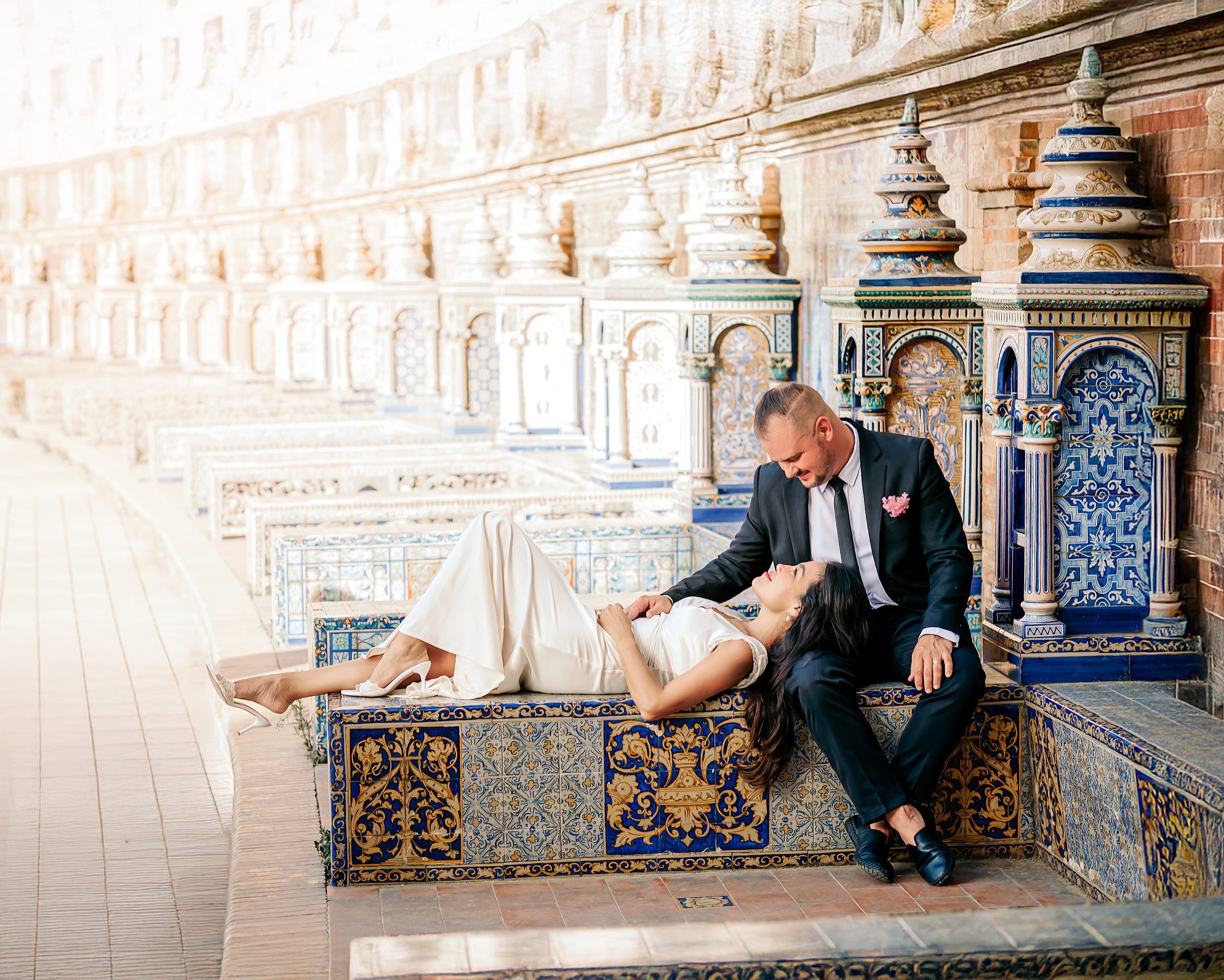 Romantic wedding photo of a couple at Plaza de España in Sevilla, Spain, with the bride resting on the groom’s lap surrounded by stunning Andalusian ceramic tiles — a perfect example of intimate and artistic wedding photoshoots in Seville.