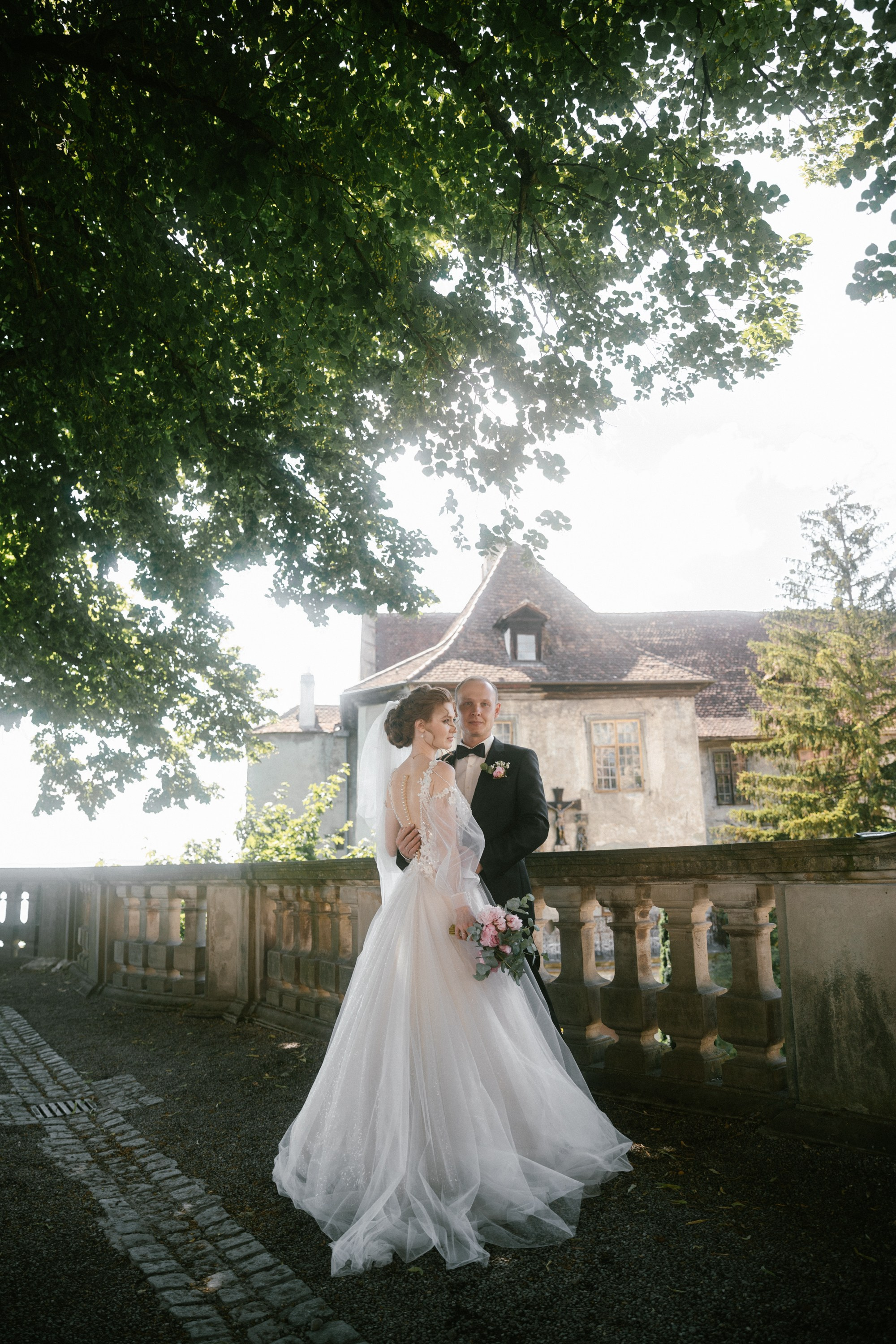 Bride and groom embrace on terrace at Schloss Meersburg, framed by nature and sunlight