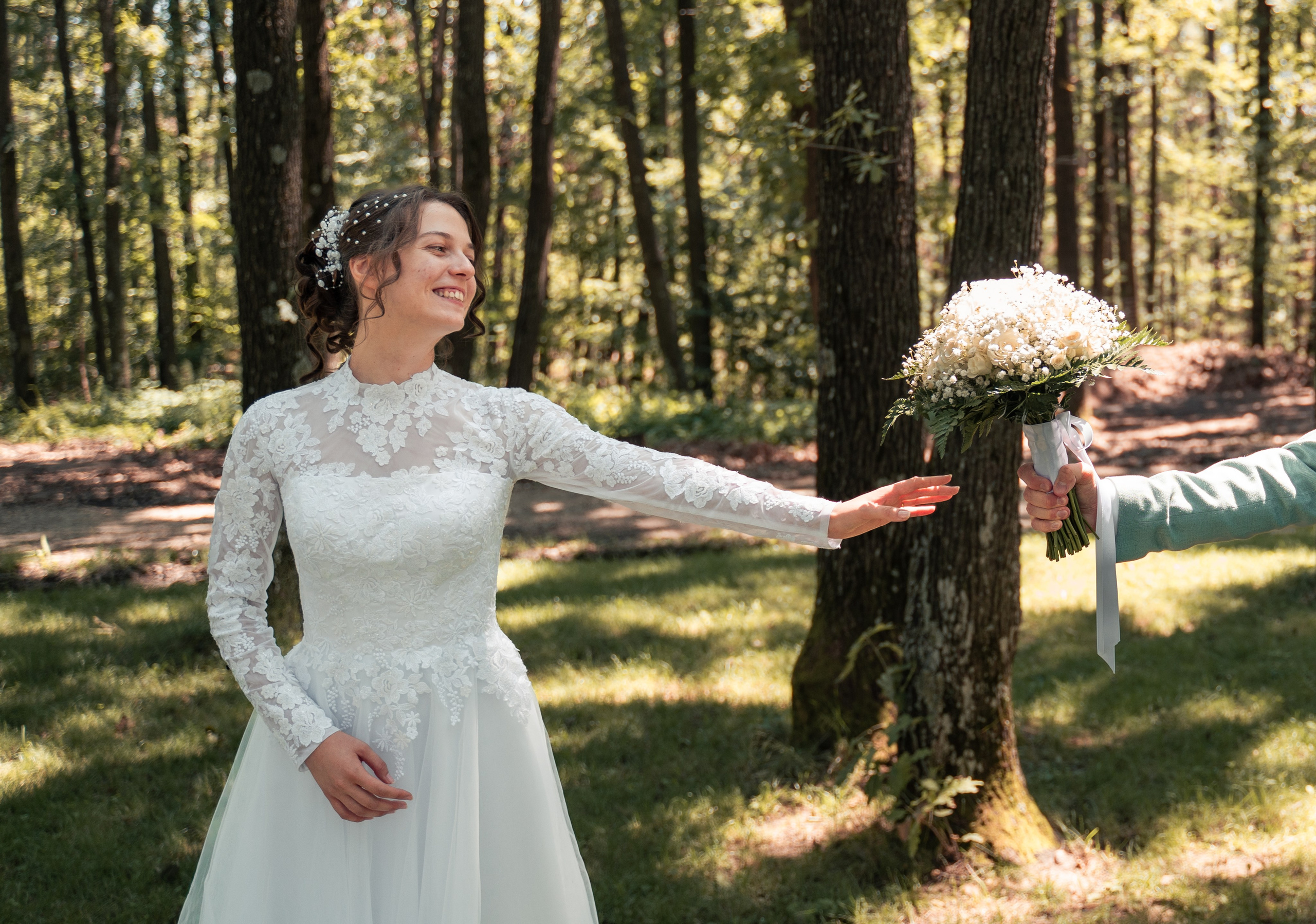 Mireasă zâmbind fericită întinzând mâna spre buchet, mire oferindu-i flori în pădure, fotografie de nuntă spontană București, incadru.ro.