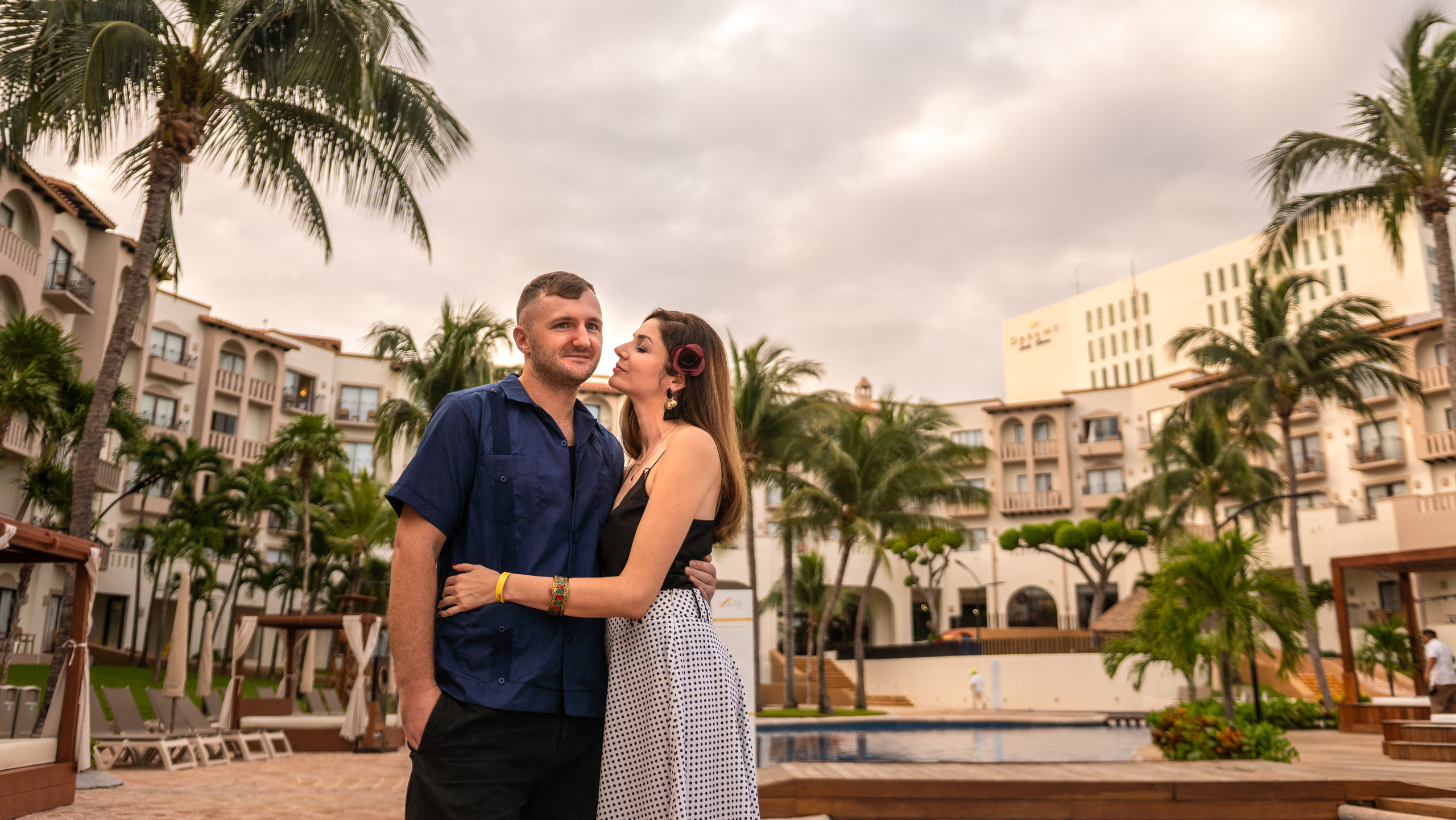 Laughing couple in white and floral outfit sitting in front of a traditional colonial hotel in Cancún, captured by a candid lifestyle photographer in Mexico
