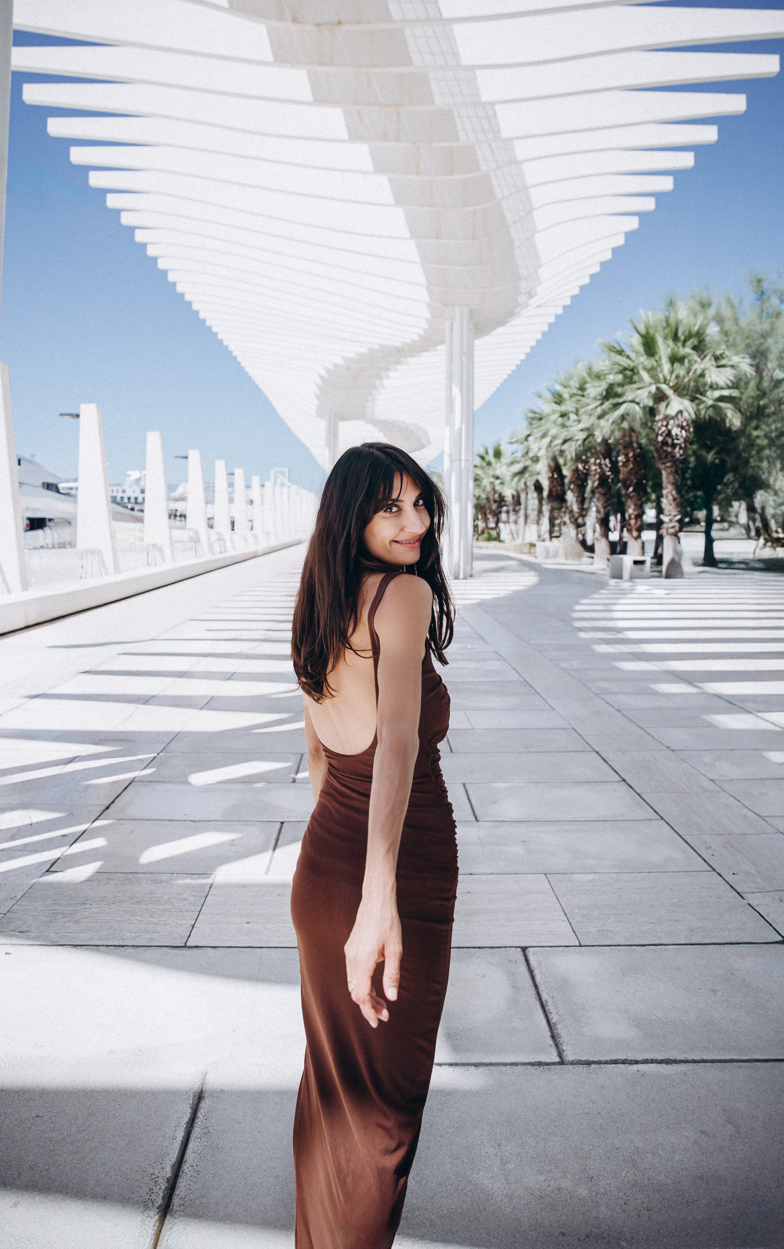 Стильная портретная фотосессия в Малаге, Испания — уверенная женщина в коричневом платье идёт под культовой перголой в районе Муэлье Уно, идеально для туристов и местных, ищущих современную и художественную портретную фотографию в Малаге и на Коста-дель-Соль.