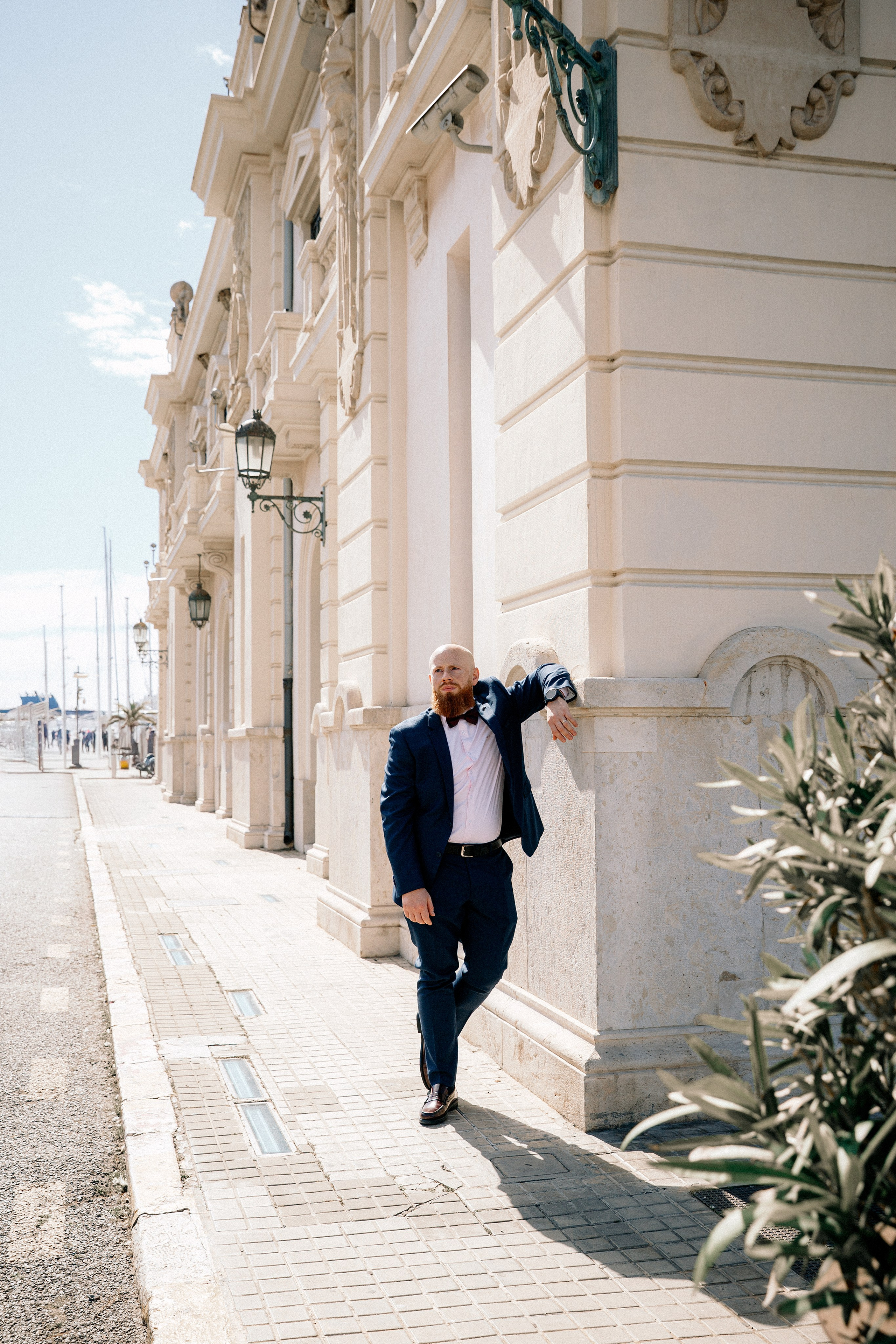 Мужская портретная фотосессия в Валенсии, Испания, со стильным мужчиной в классическом чёрном костюме, опирающимся на элегантное историческое здание с изысканной архитектурой, снятым при мягком естественном дневном свете, создающим утончённое и уверенное городское настроение — идеально для мужской портретной фотографии, lifestyle-фотосессий для мужчин, портретов для персонального бренда, editorial-съёмок и профессиональных мужских фотосессий в Валенсии и по всей Испании.